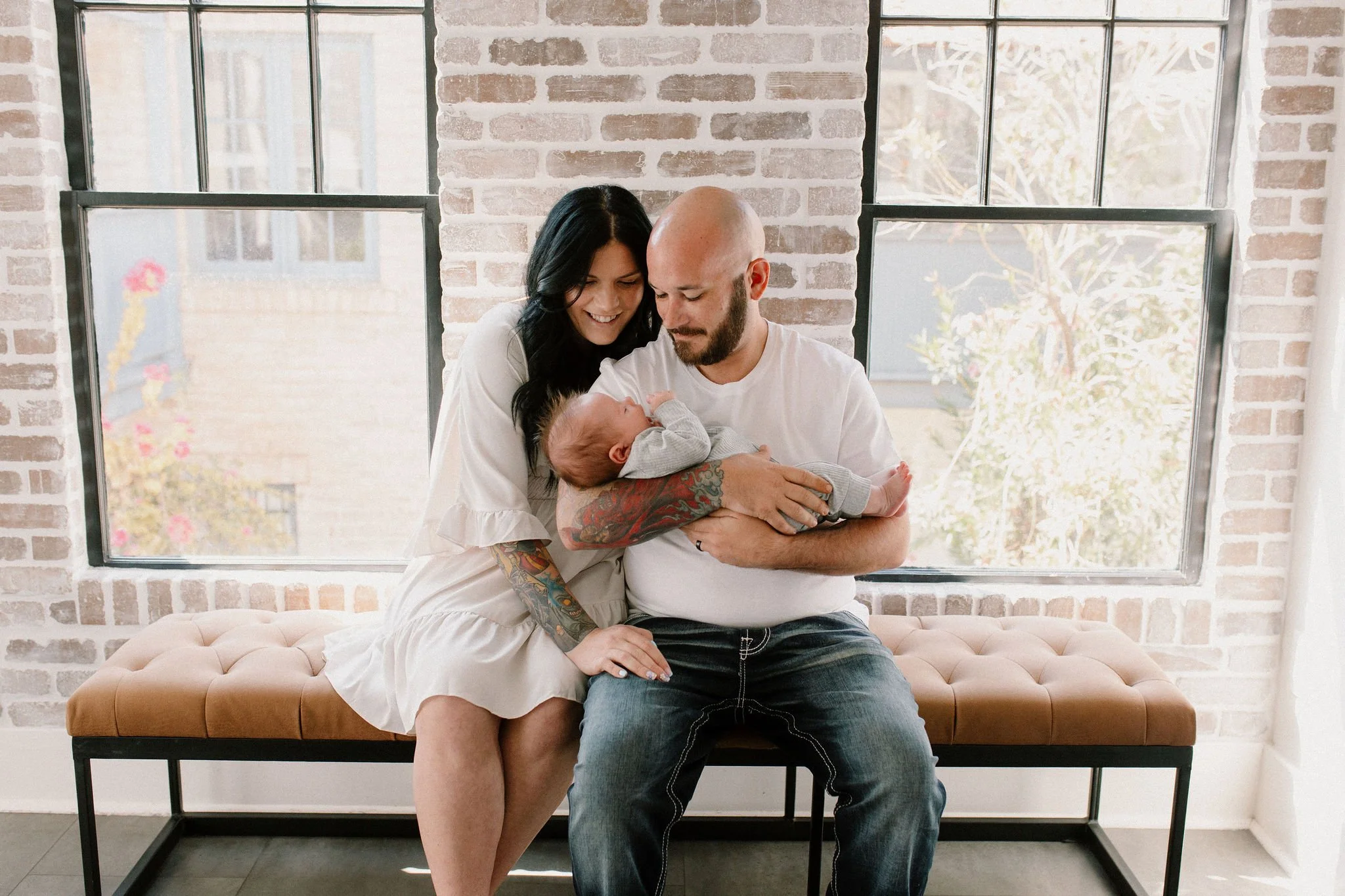 mom and dad holding baby in front of windows in natural light studio by Phoenix newborn photographer