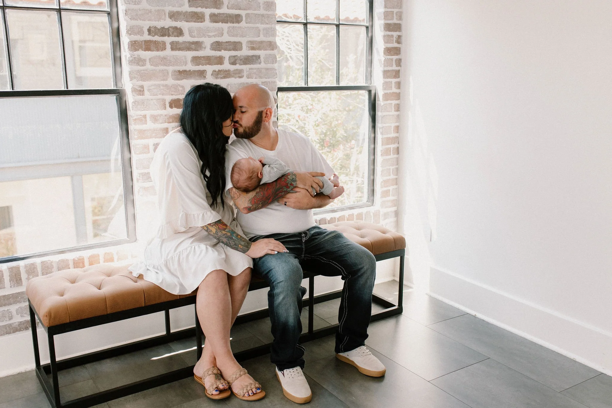 mom and dad kissing while holding baby in natural light studio by Phoenix newborn photographer