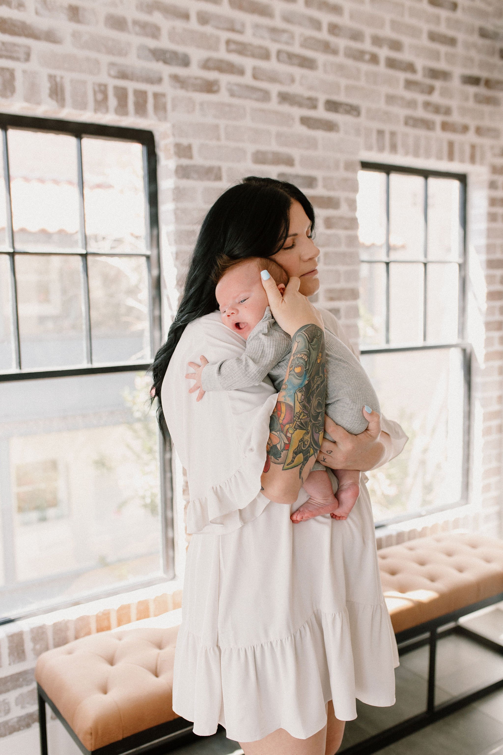 mom holding baby in front of windows in natural light studio by Phoenix newborn photographer