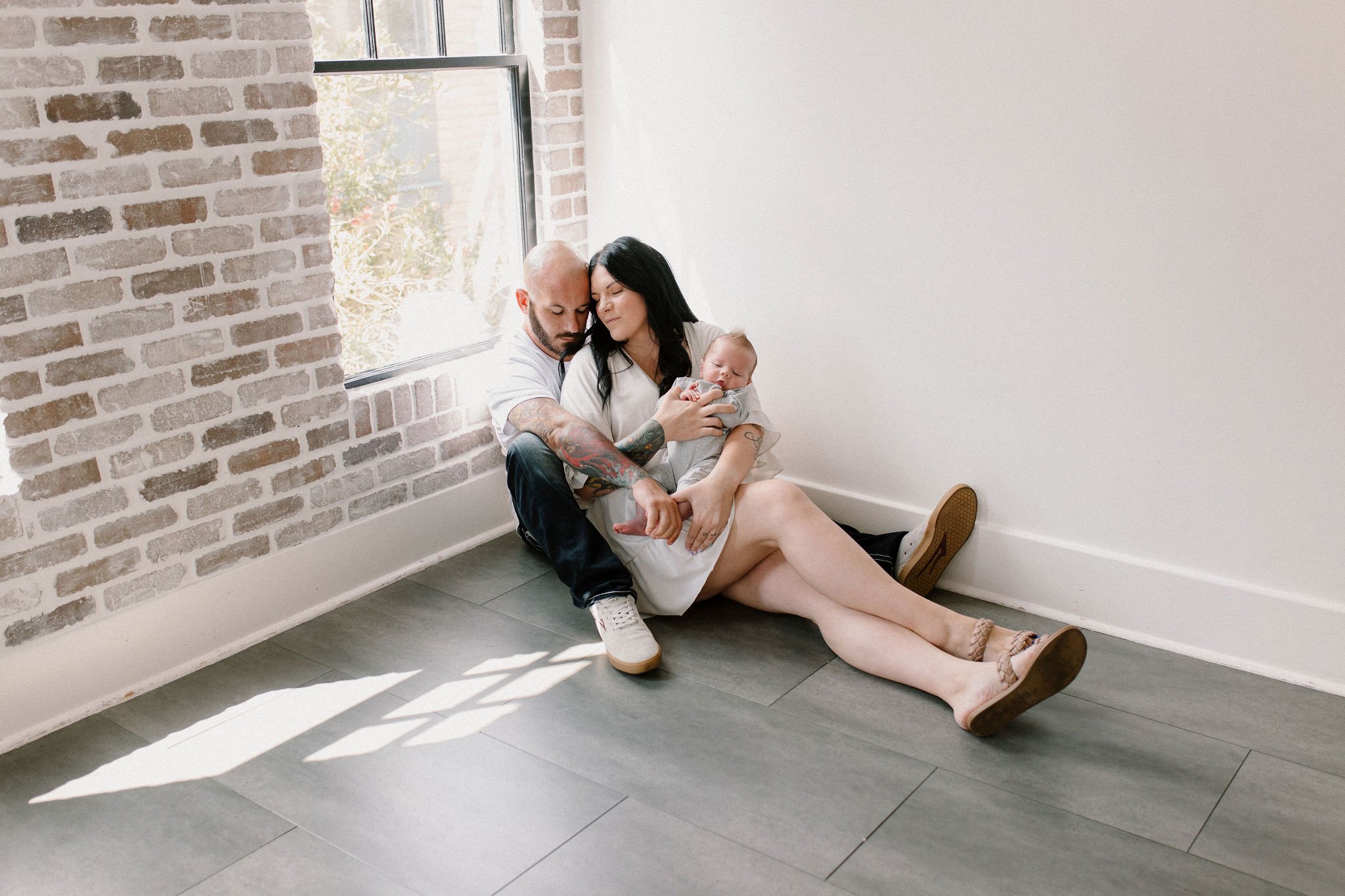 phoenix newborn photographer captures mom and dad cuddling while holding newborn baby in natural light studio session