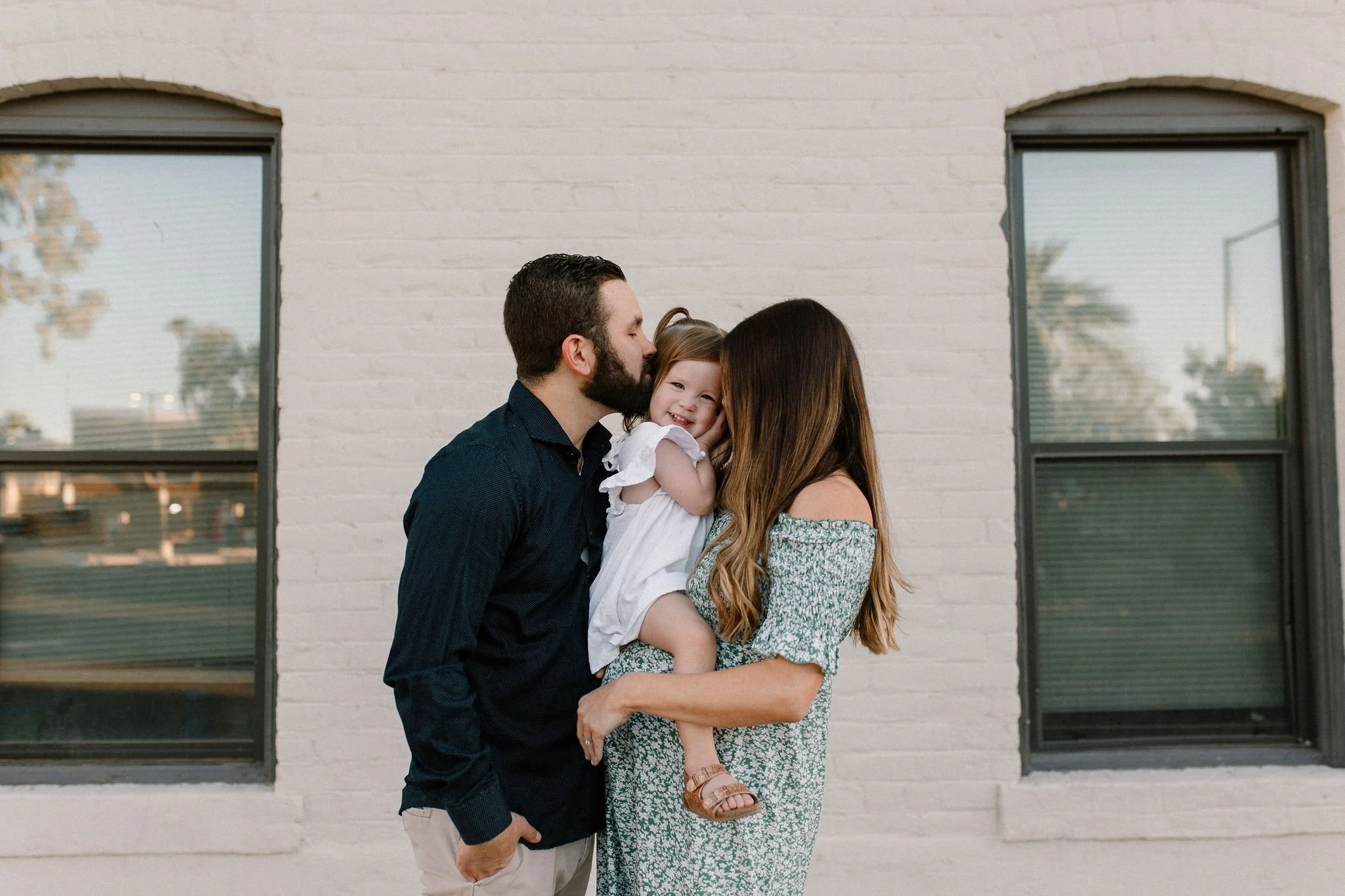pregnant mom and dad holding daughter kissing cheeks in maternity photoshoot Gilbert, Arizona