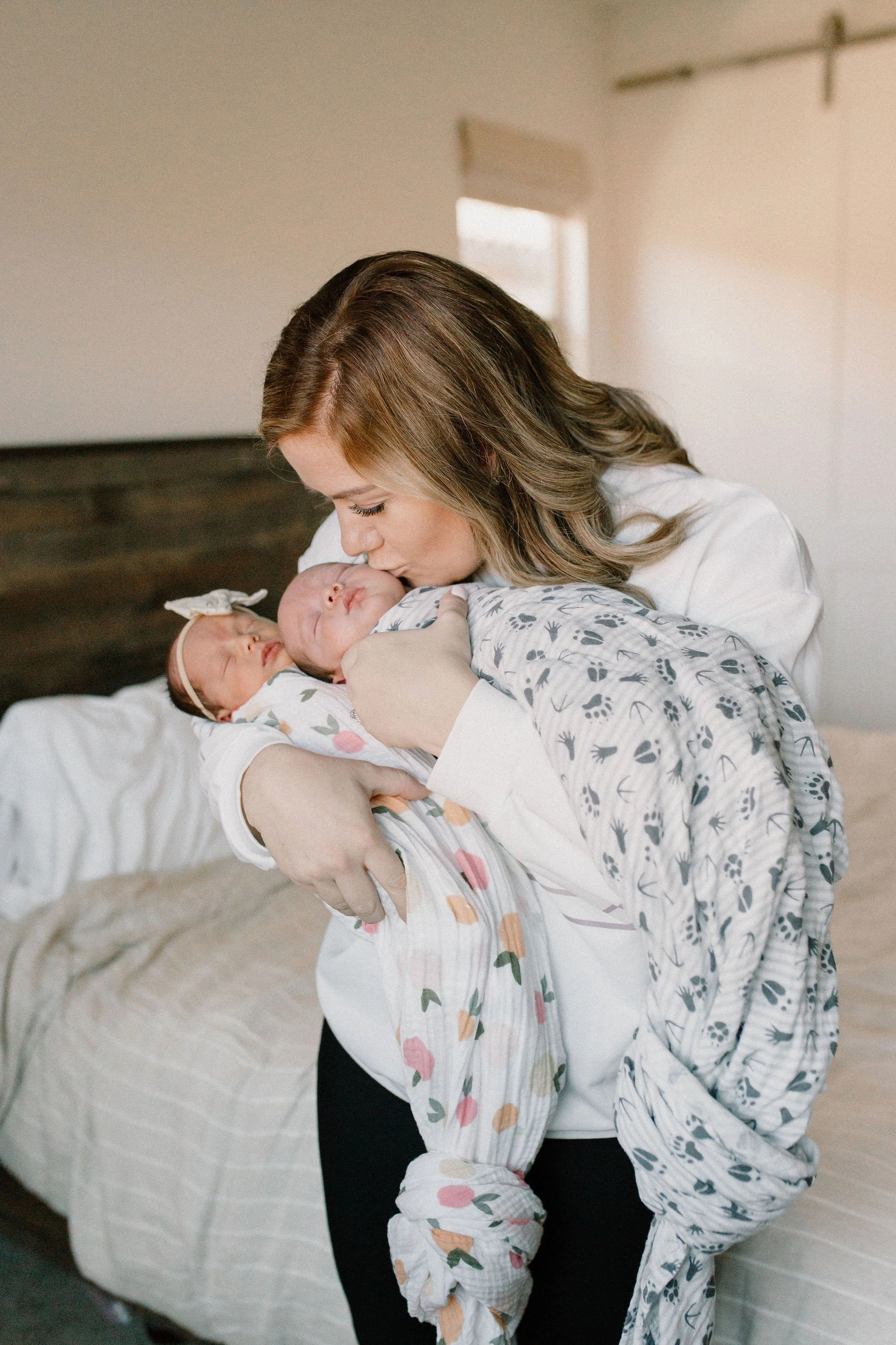 mom holding and kissing swaddled newborn twin babies