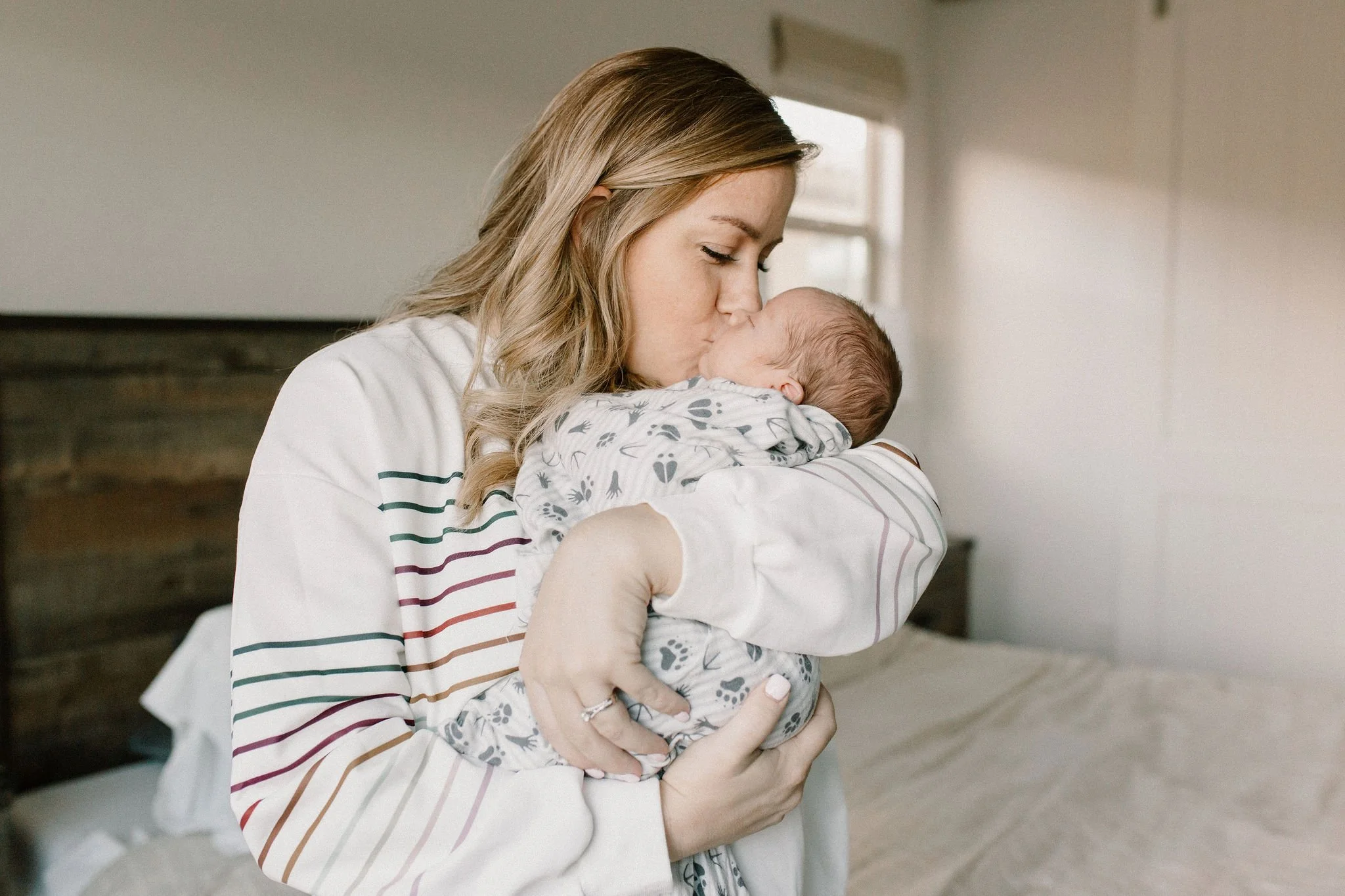 mom holding and kissing swaddled newborn baby boy