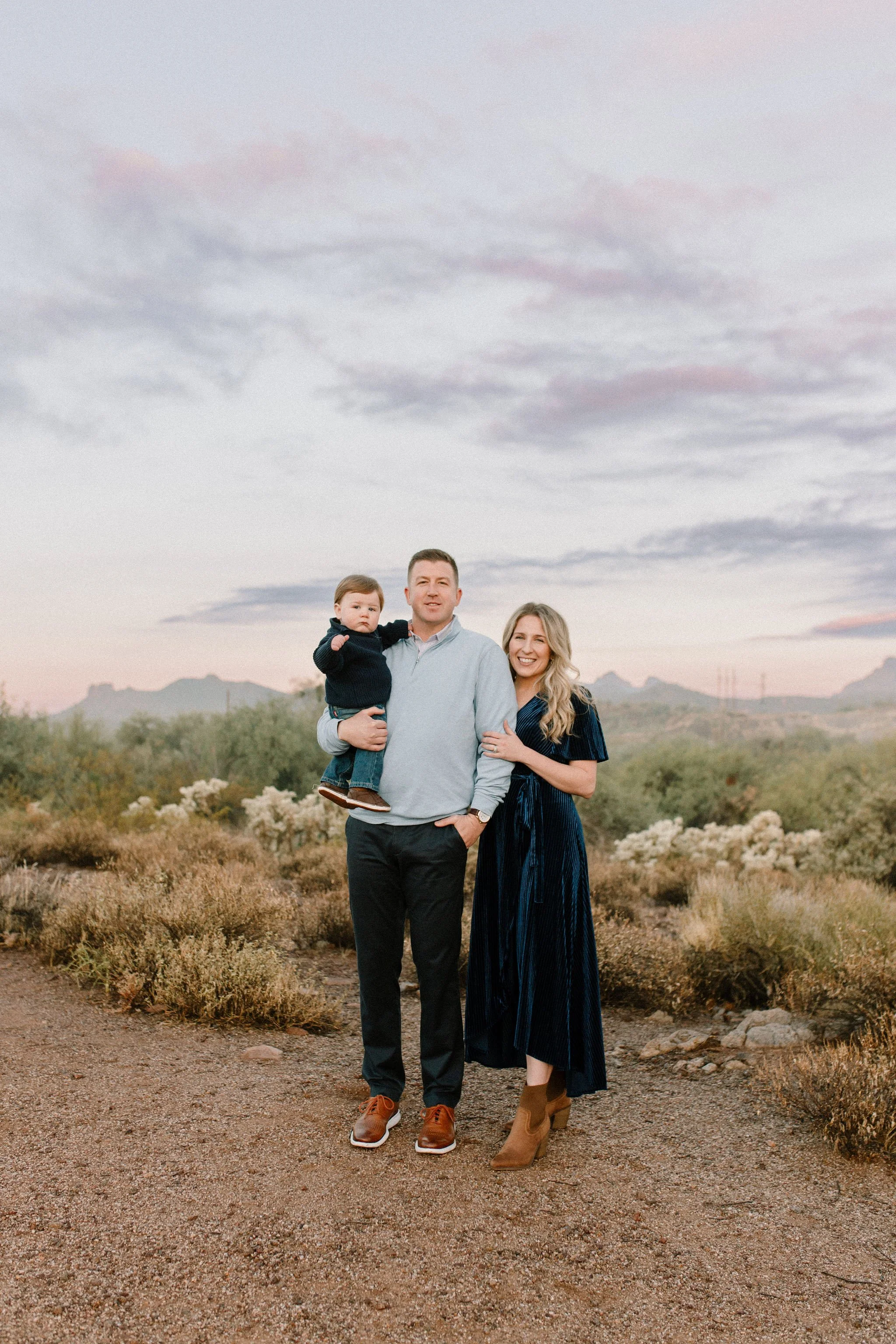family of three standing together and smiling in desert during blue hour