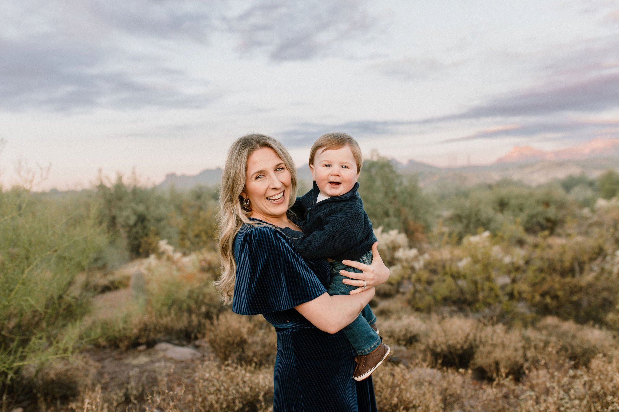 mom and baby boy standing in the desert and smiling during blue hour