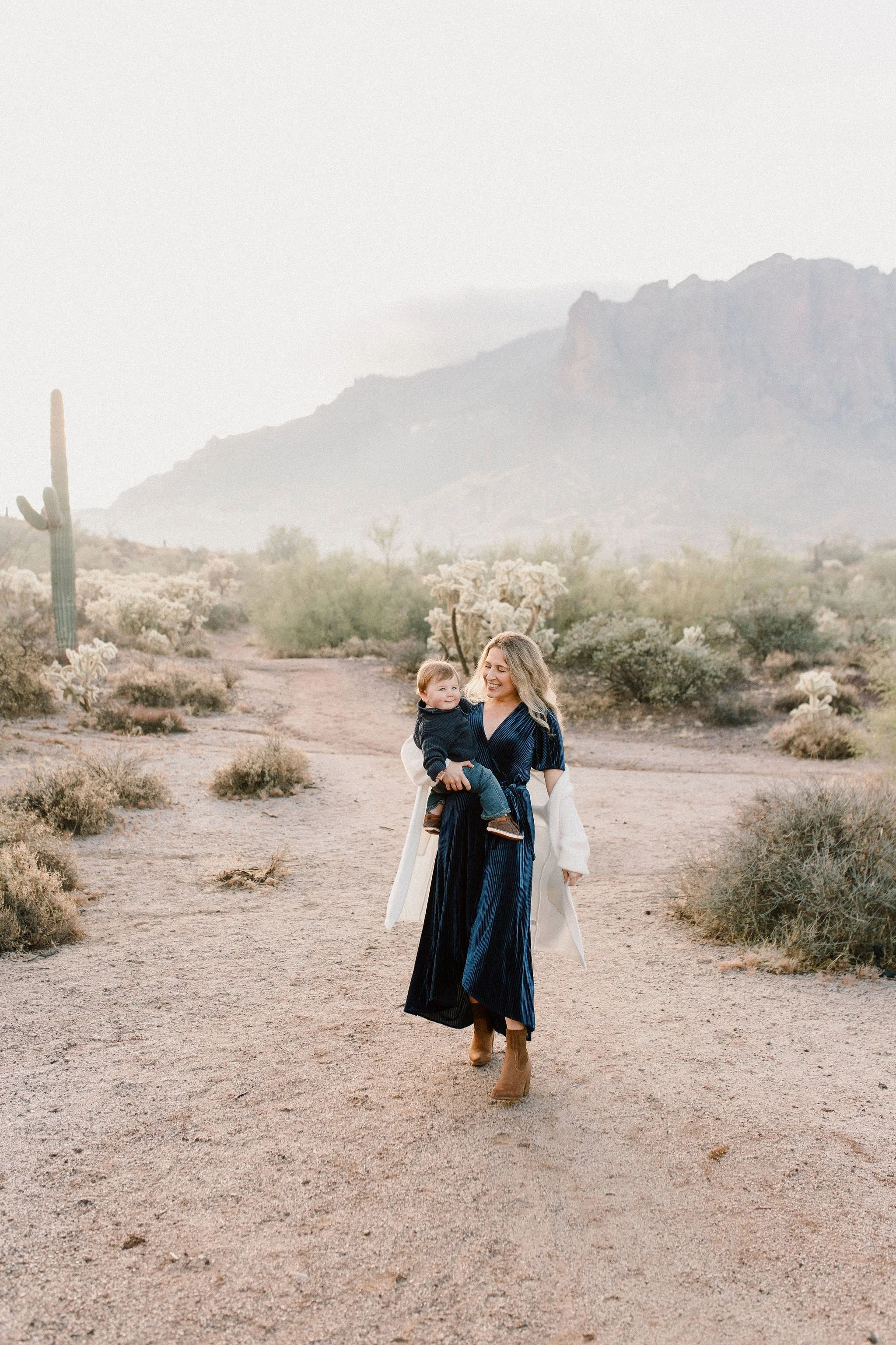 mom walking with baby boy in desert during misty morning photography session at the Superstition Mountains in Arizona