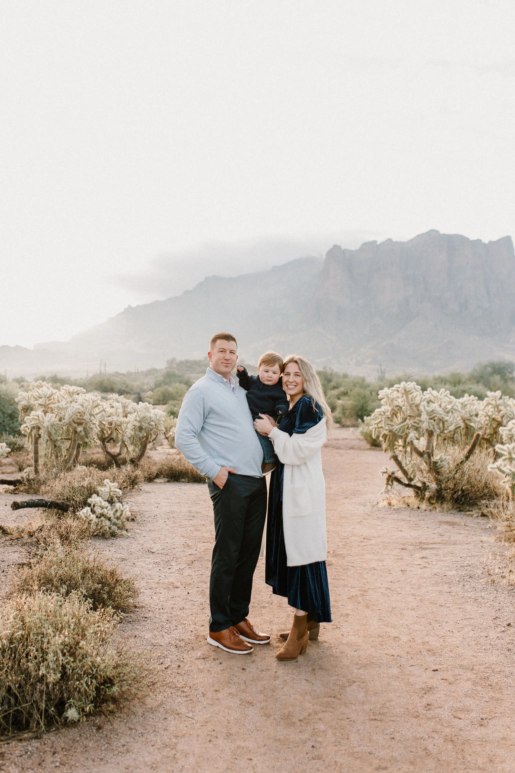 Family of three standing together and smiling in the desert during misty morning photography session at the Superstition Mountains in Arizona