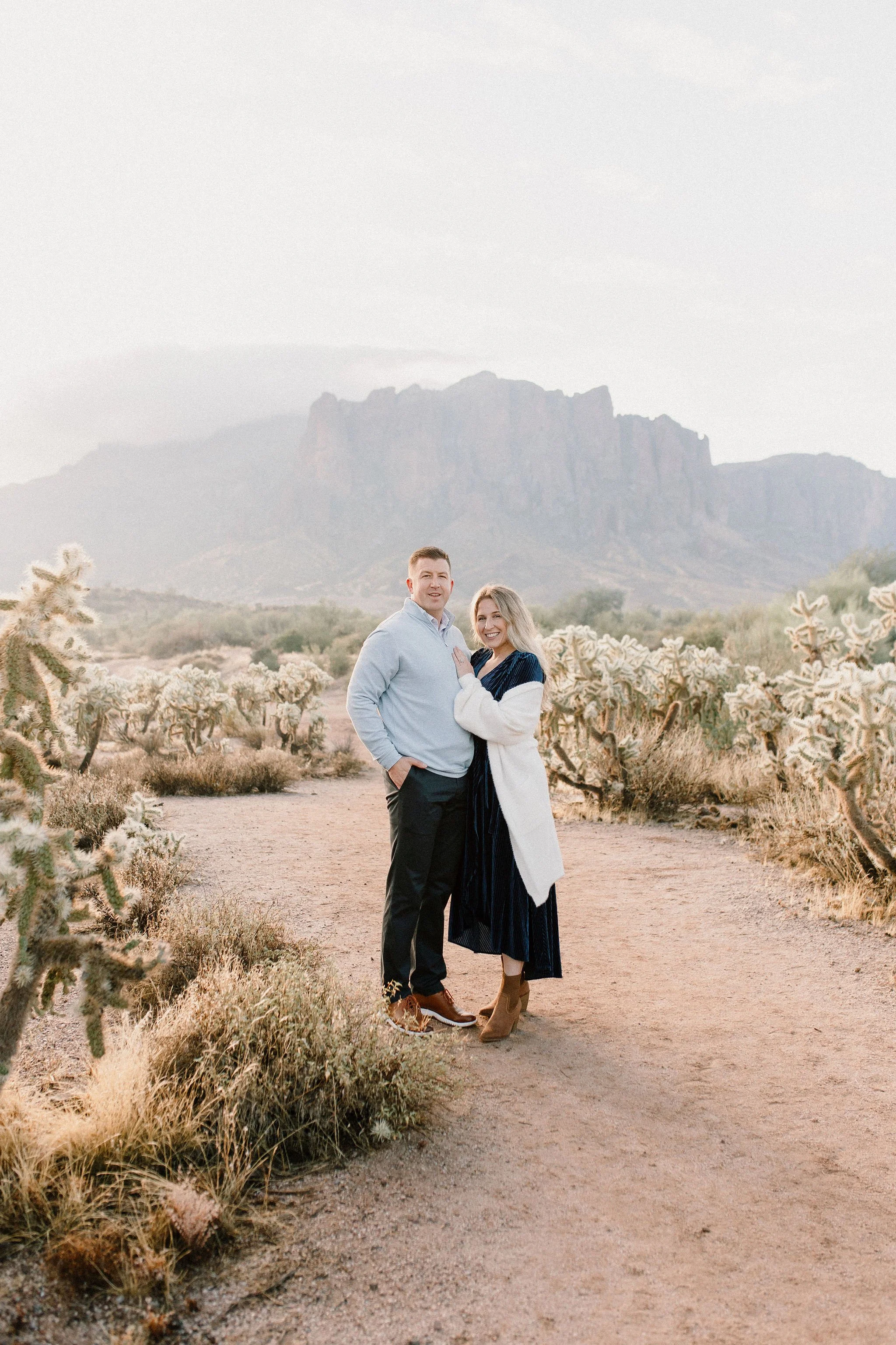 mom and dad standing together smiling in the desert during misty morning family session at Superstition Mountains in Arizona