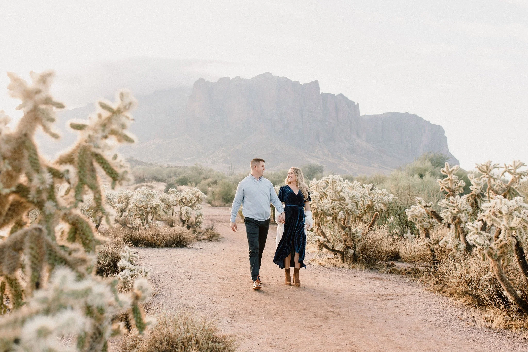mom and dad walking and smiling at each other in the desert in misty morning family photography session at the Superstition Mountains in Arizona