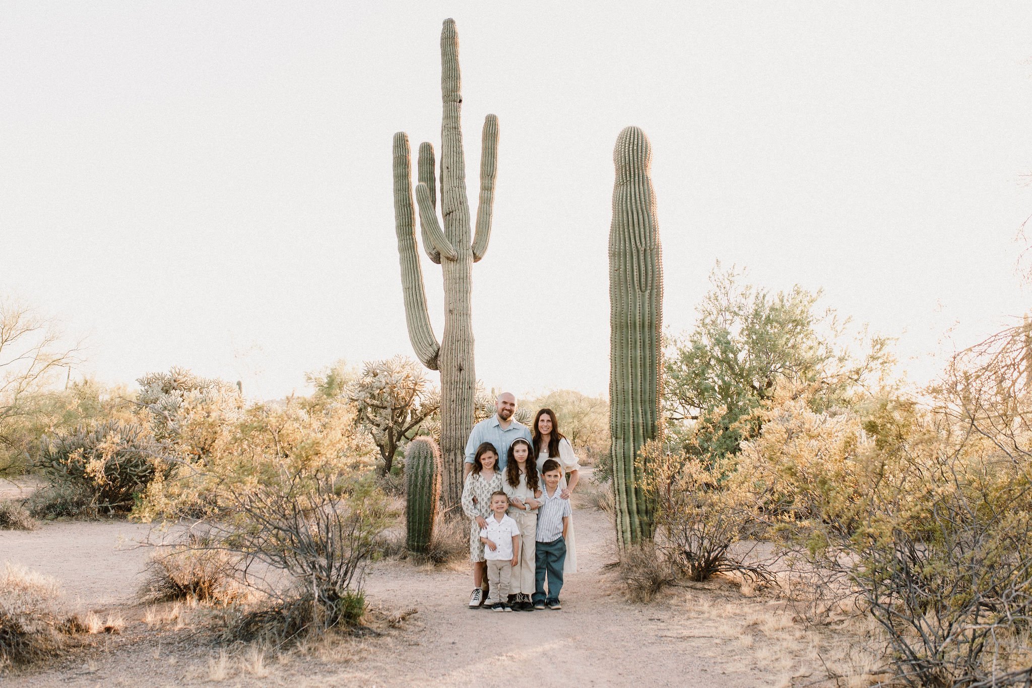 family smiling in front of giant saguaro cactus in Arizona desert taken by Mesa family photographer