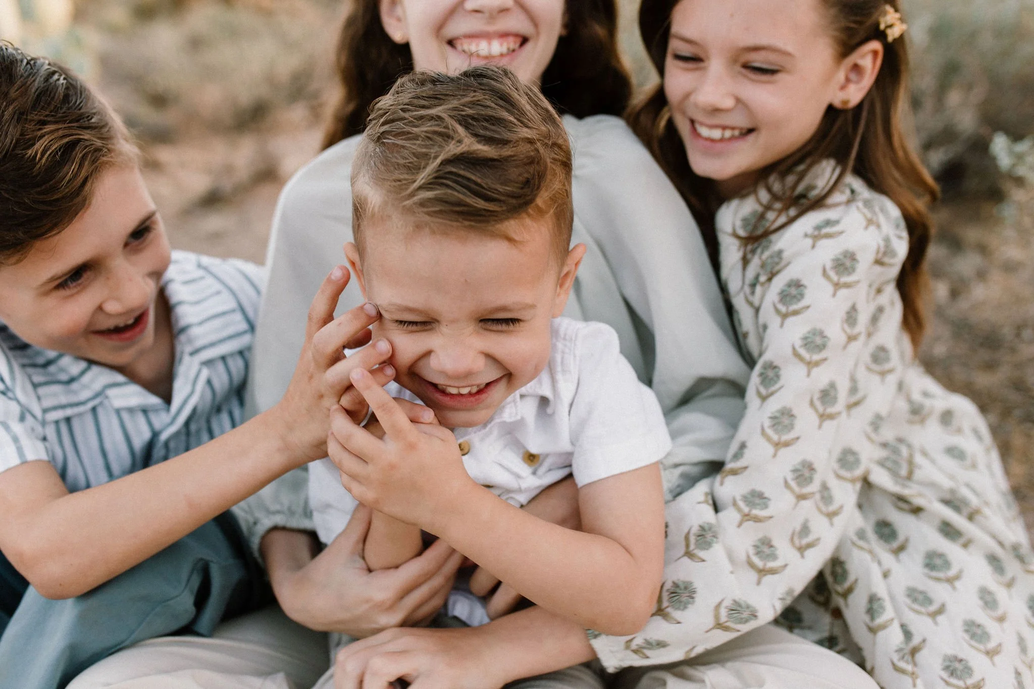 siblings tickling youngest captured by Mesa family photographer in Arizona desert