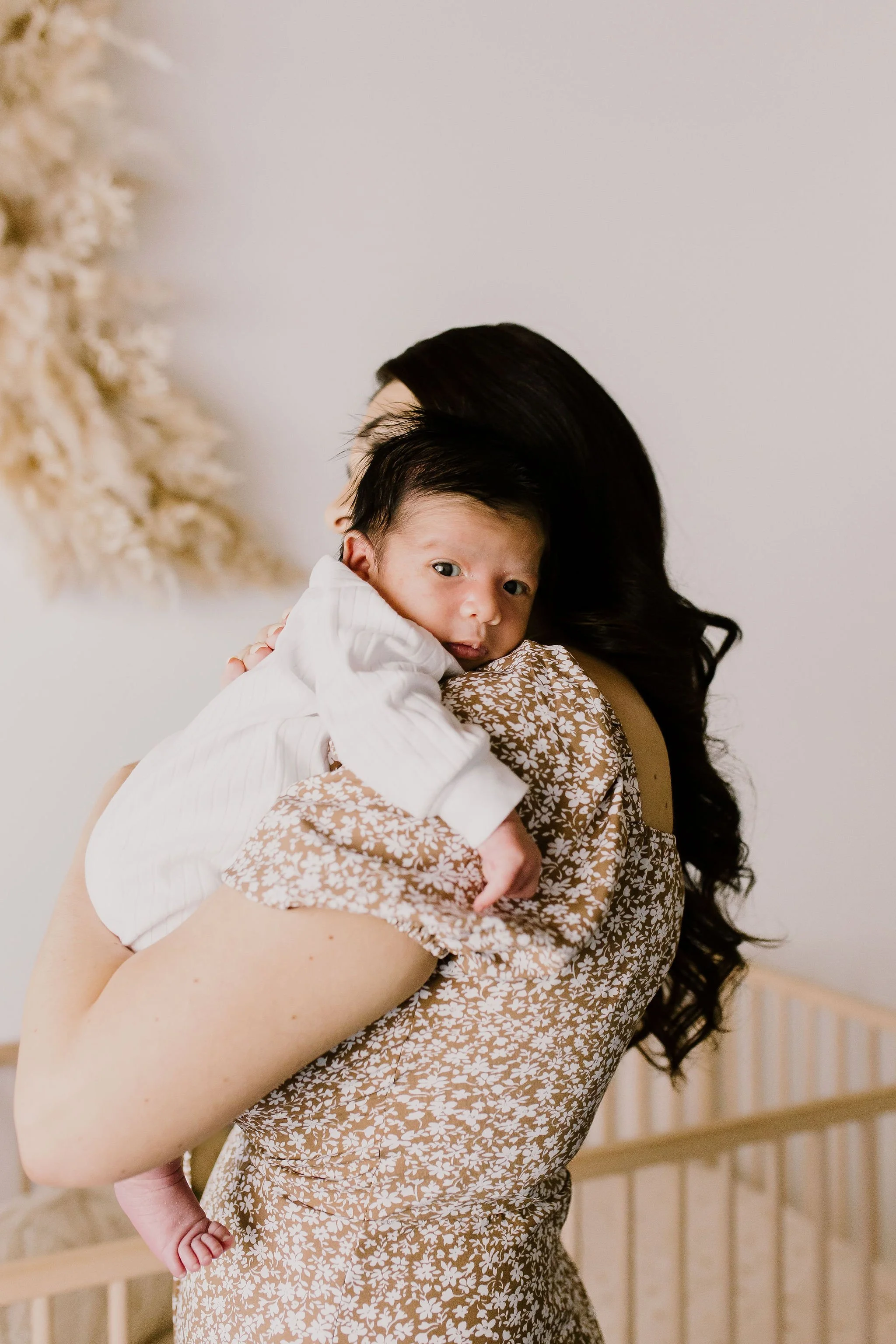 mom holding baby standing in nursery for studio newborn photography