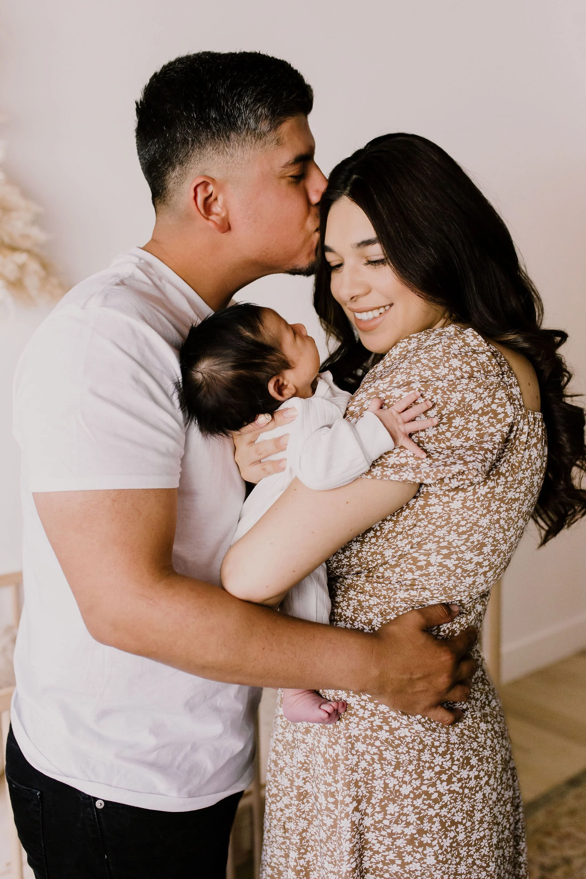 dad kissing mom's forehead while mom holds baby in studio newborn photography session