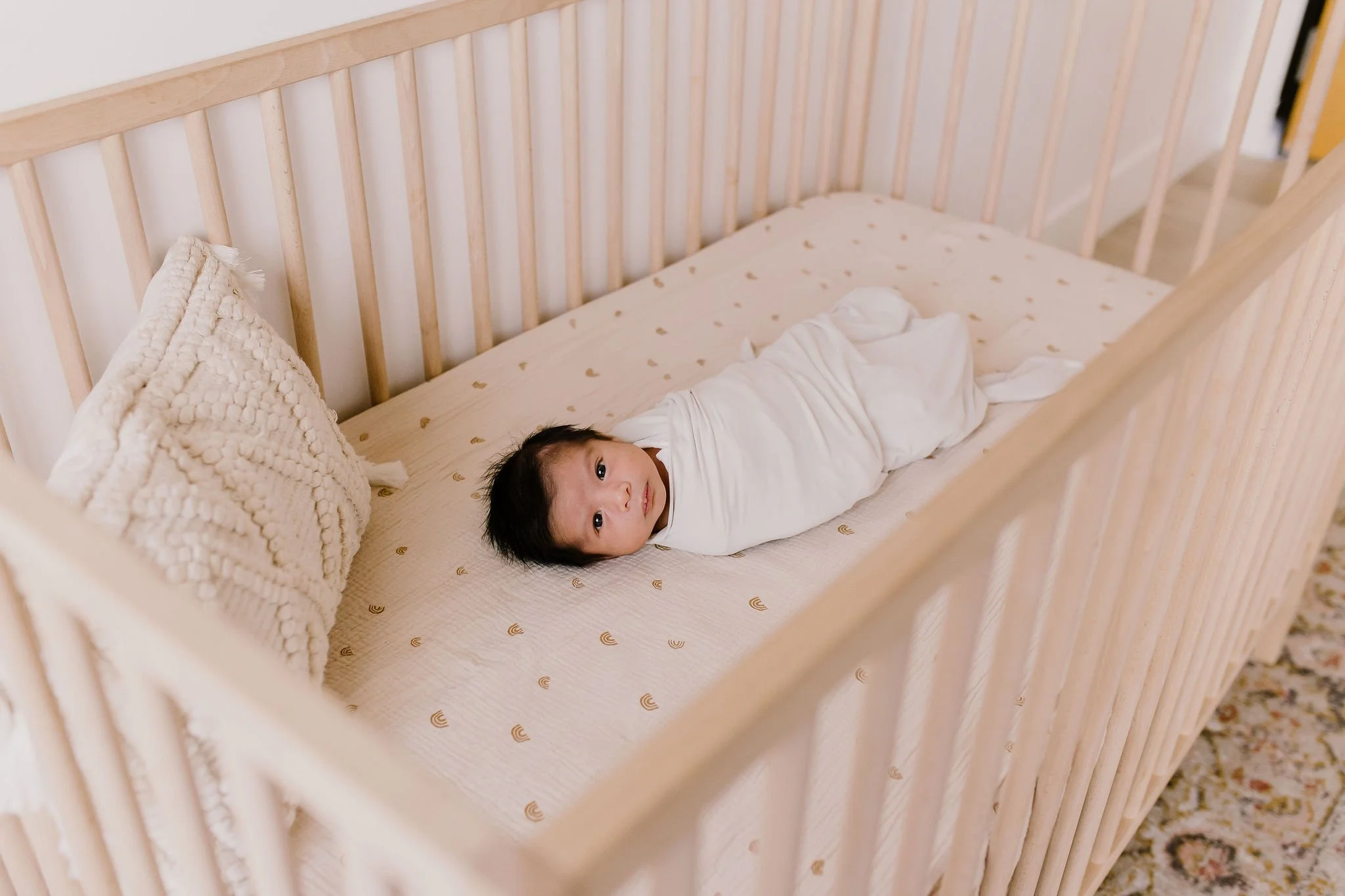 swaddled baby laying in crib looking at the camera in studio newborn photography session