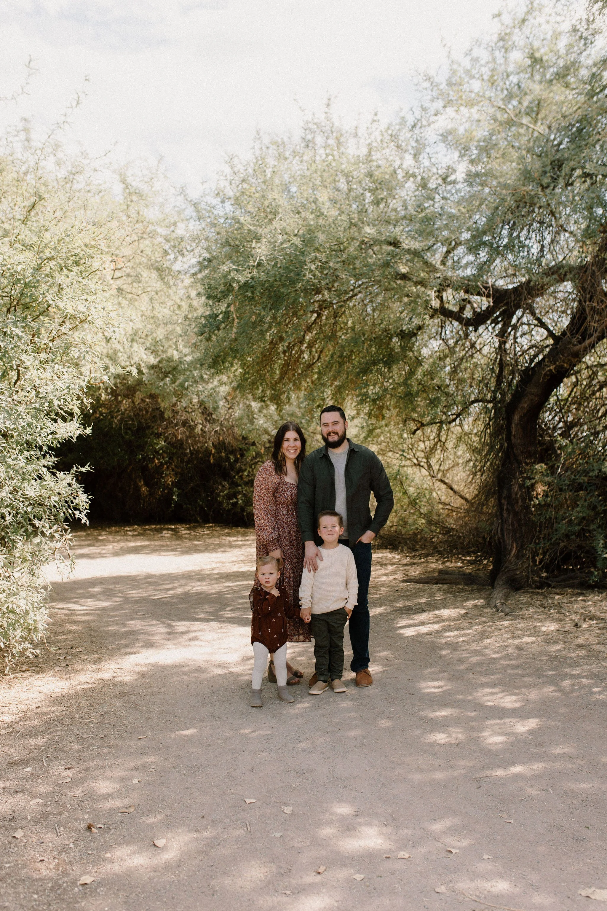 family standing in desert greenery at Gilbert Riparian Preserve smiling at Gilbert Arizona family photographer