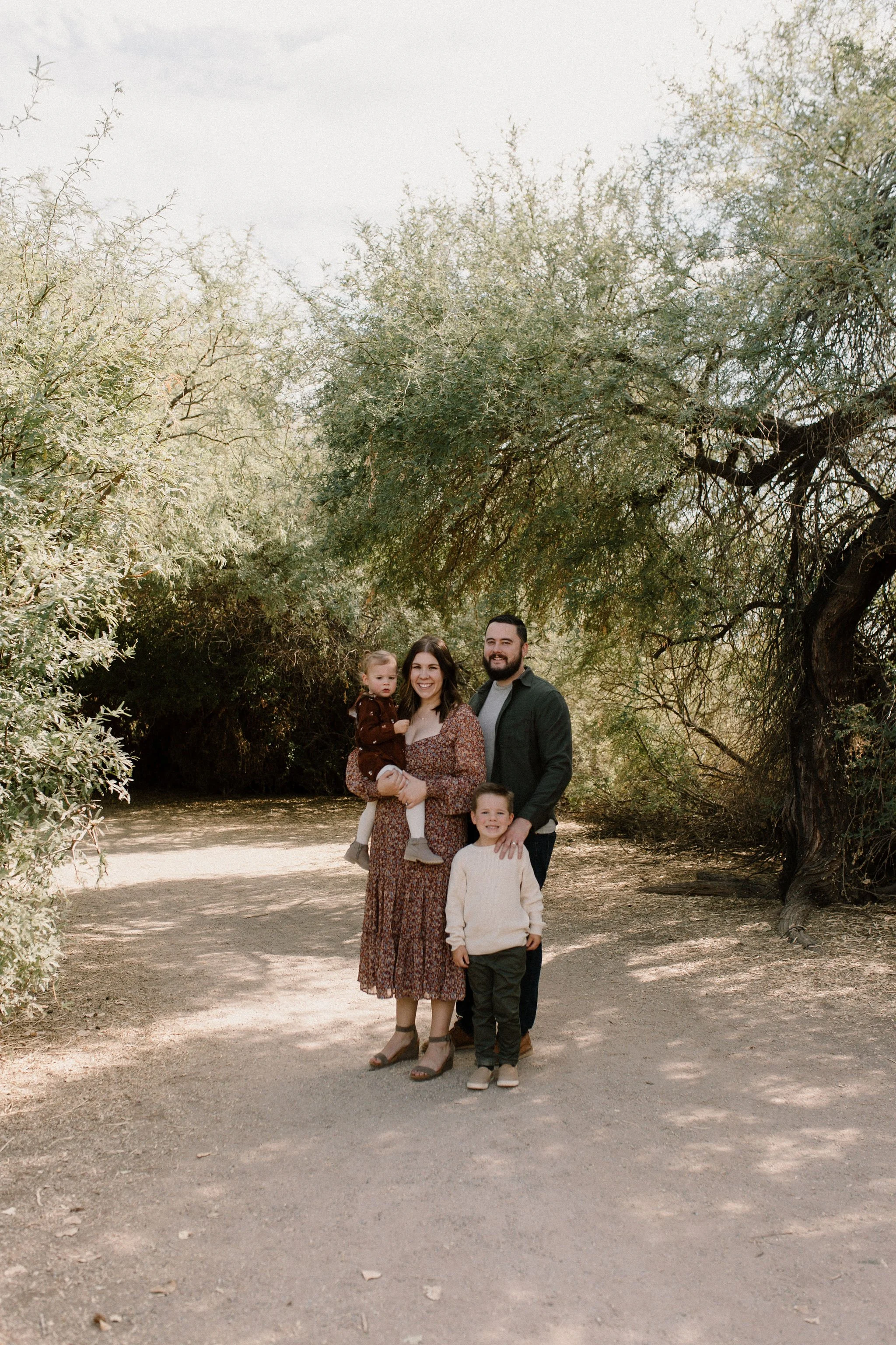 family standing in green trees smiling at Gilbert Arizona family photographer