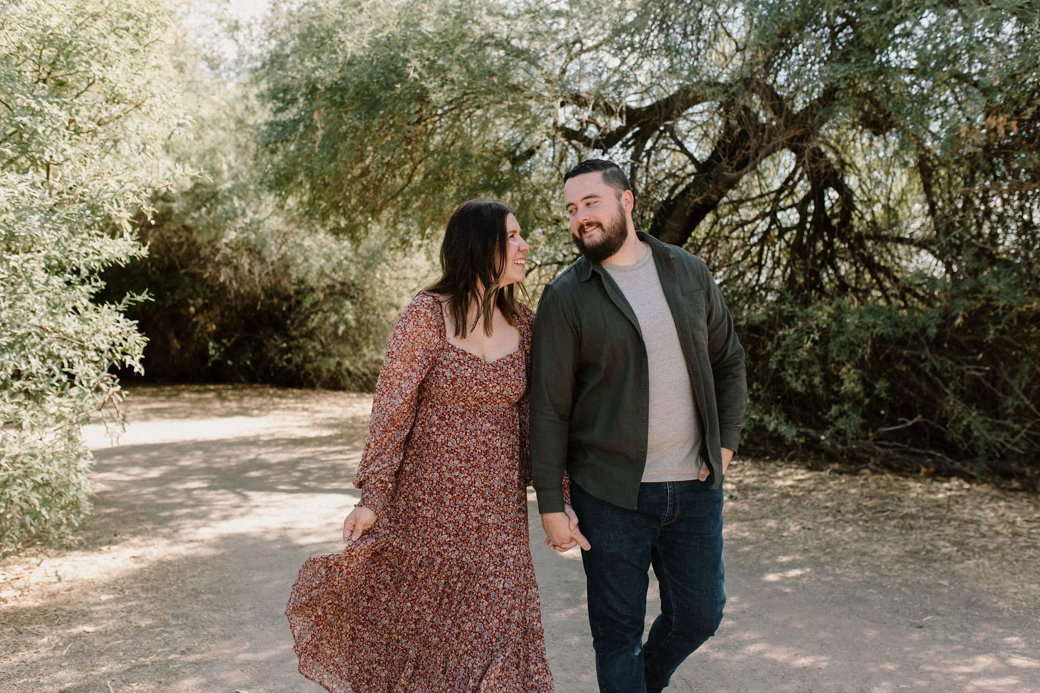 mom and dad holding hands walking in desert greenery captured by Gilbert Arizona family photographer