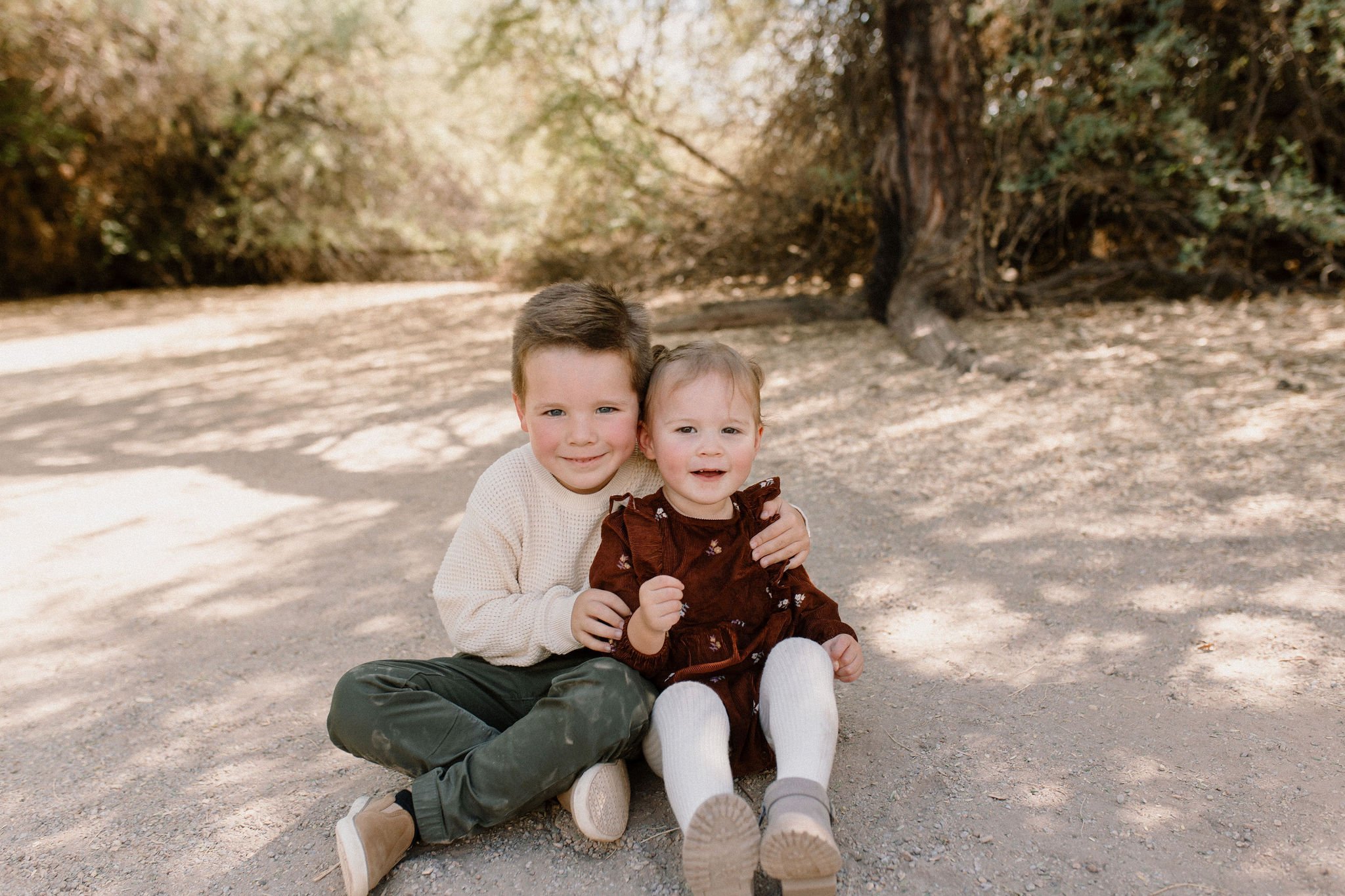 brother and sister siblings sitting in Gilbert Riparian Preserve smiling at Gilbert Arizona family photographer