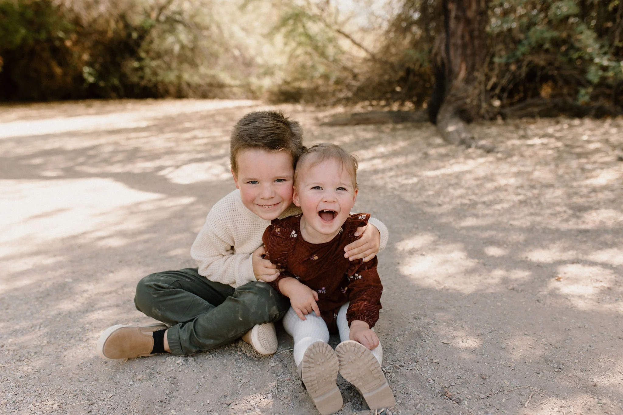 brother and sister siblings sitting in Gilbert Riparian Preserve laughing at Gilbert Arizona family photographer
