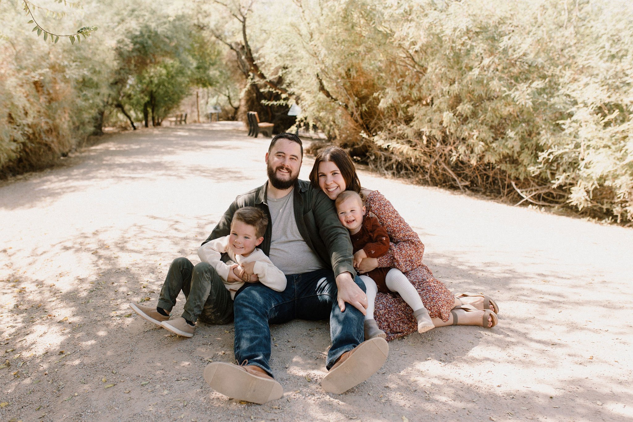 family sitting in desert greenery at Gilbert Riparian Preserve smiling at Gilbert Arizona family photographer