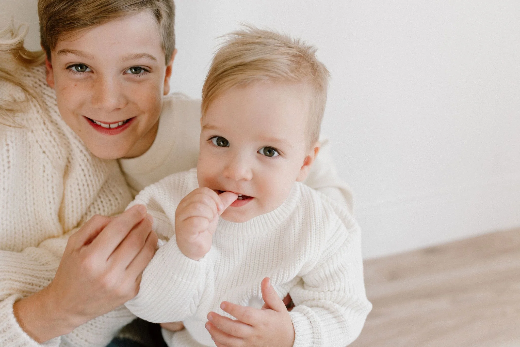 toddler sitting with mom and brother in neutral studio space