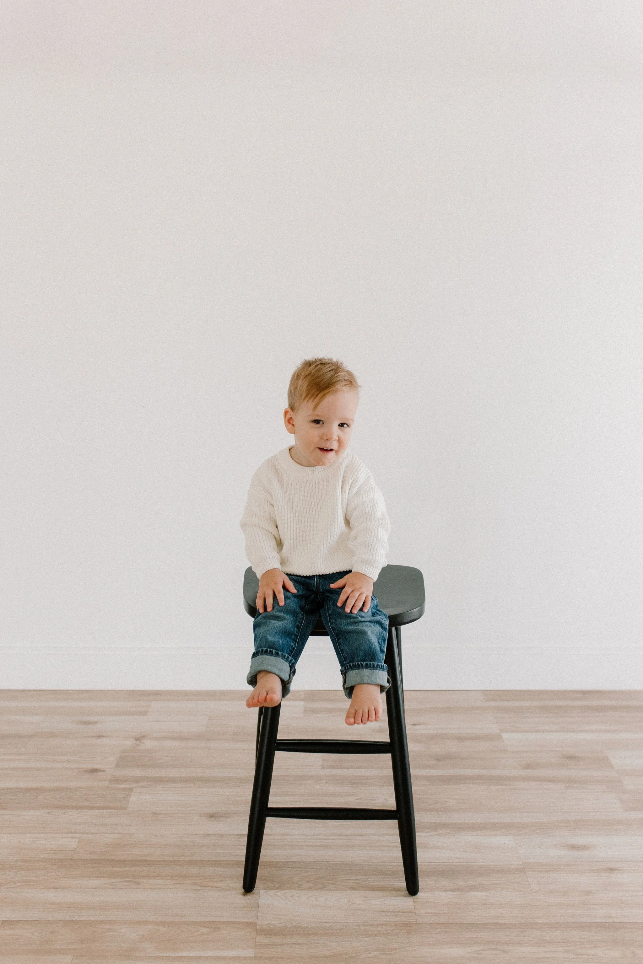 Toddler sitting on a stool in a neutral studio space