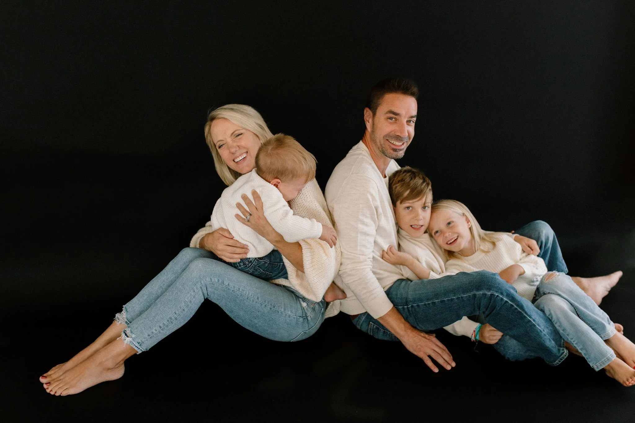 family of five sitting together against a black background in a neutral studio space