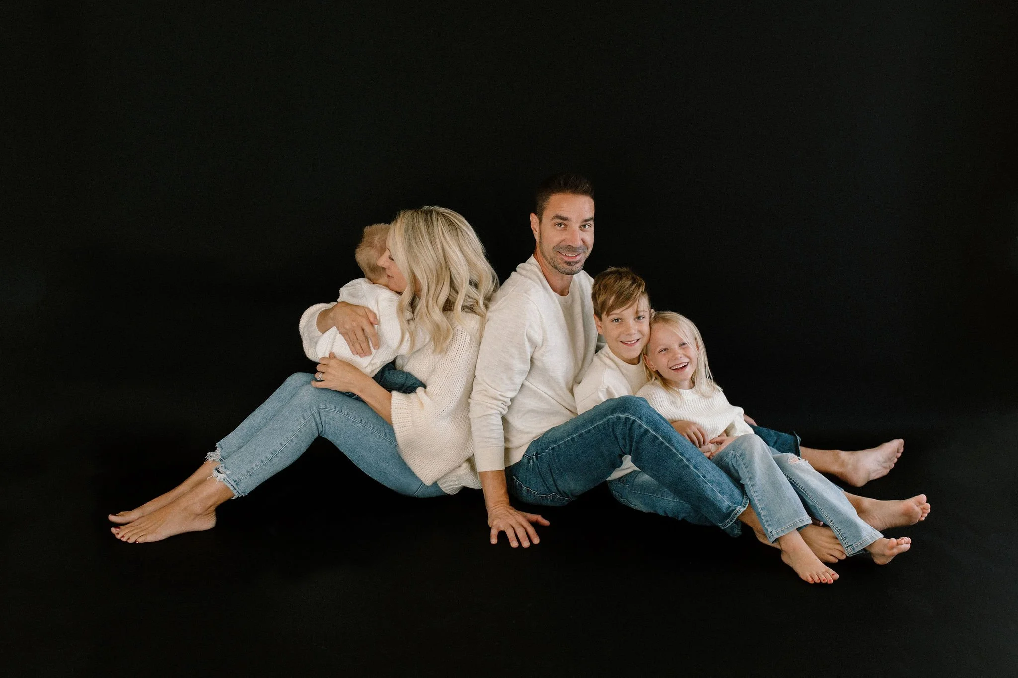 family of five sitting together against a black background in a studio space