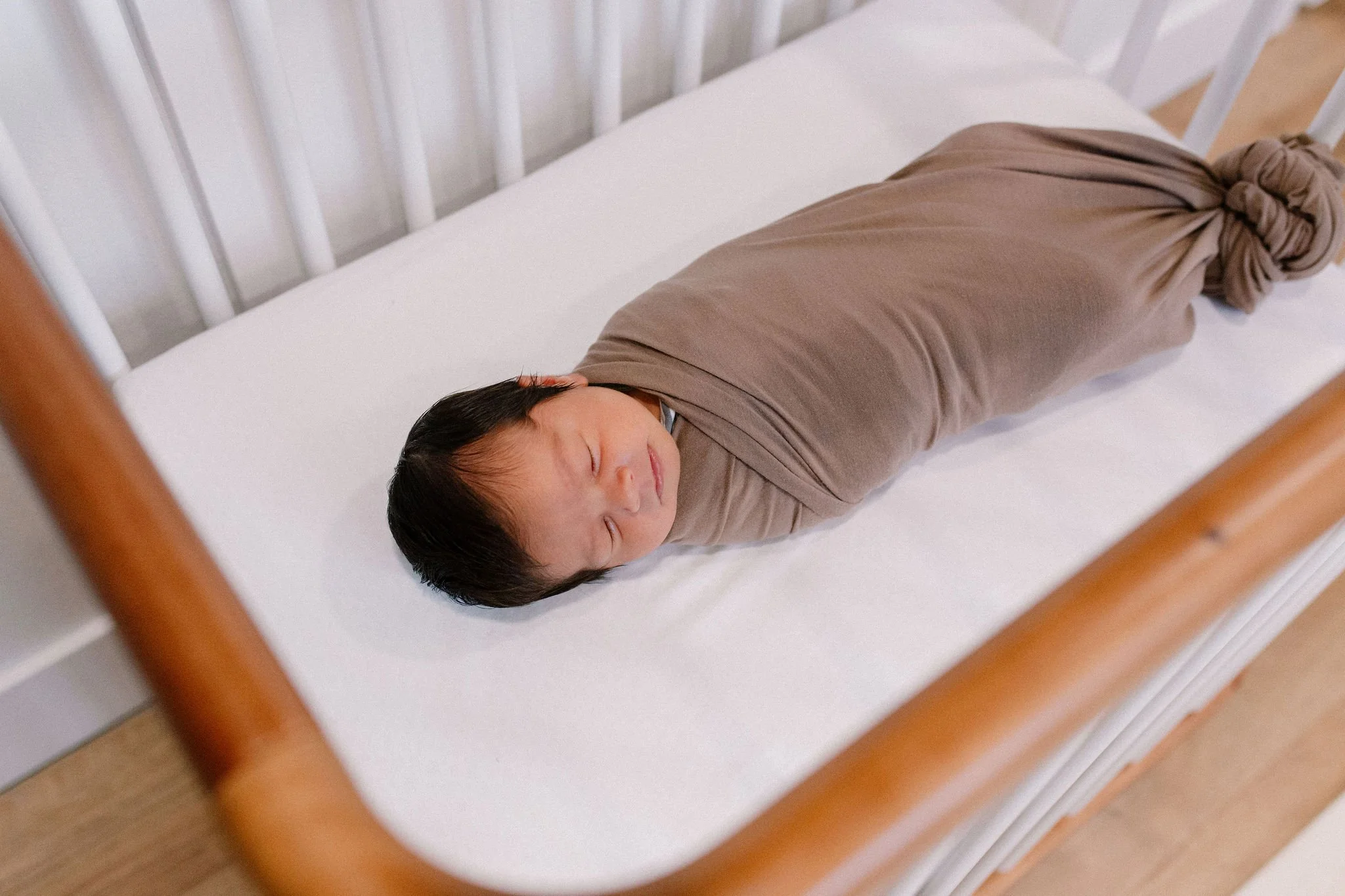 newborn baby swaddled and sleeping in bassinet in neutral nursery