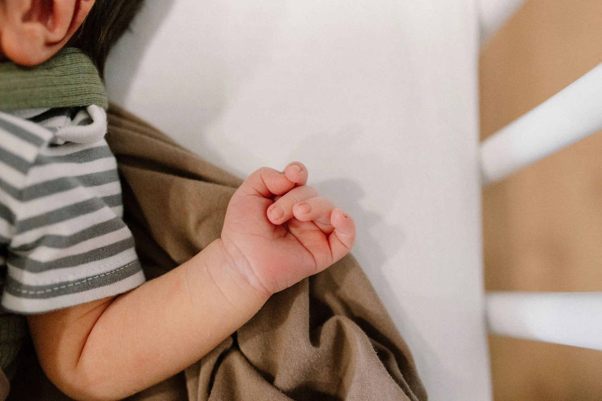 close-up photo of newborn baby fingers and hands in neutral bassinet