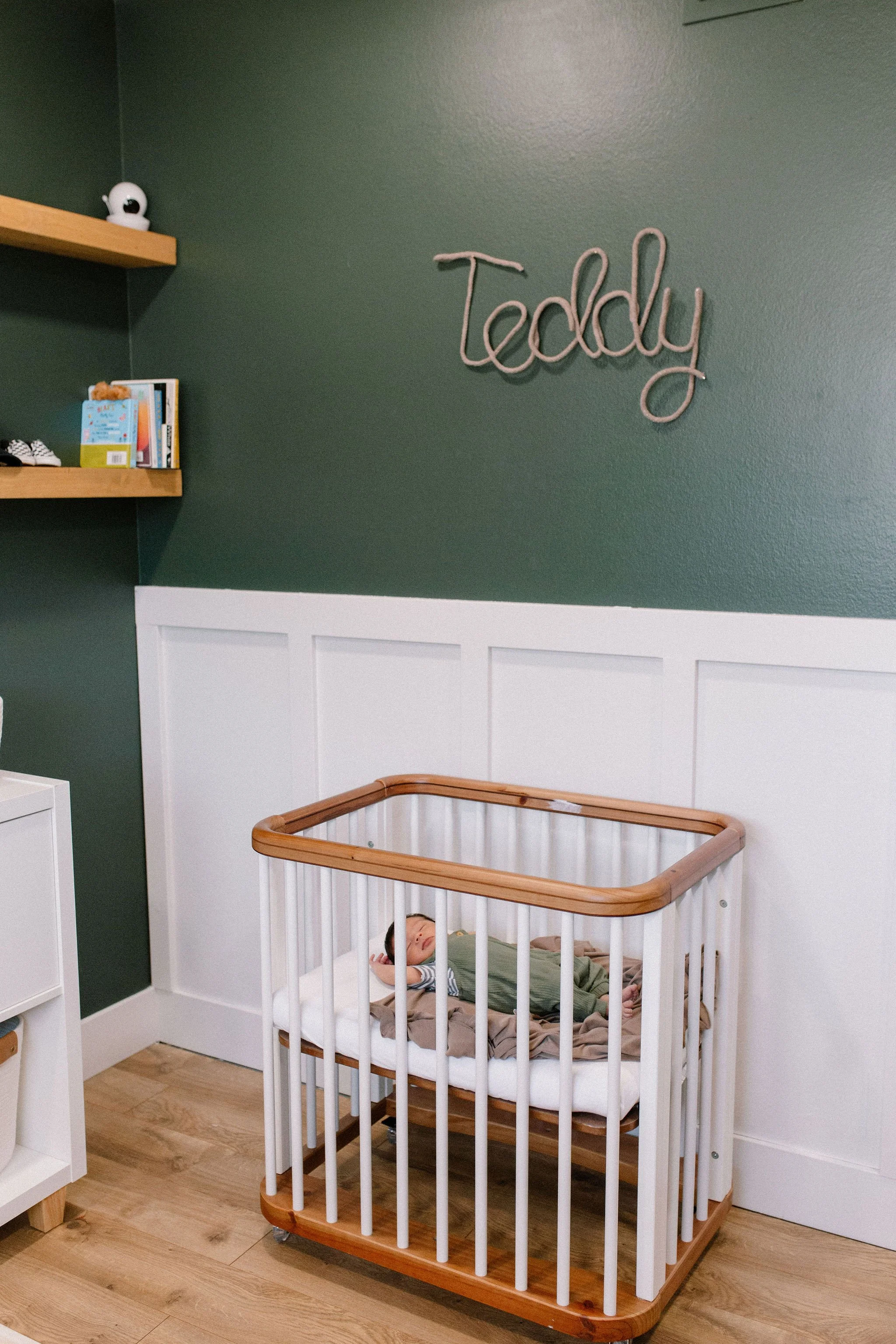 newborn baby sleeping in bassinet in dark green nursery