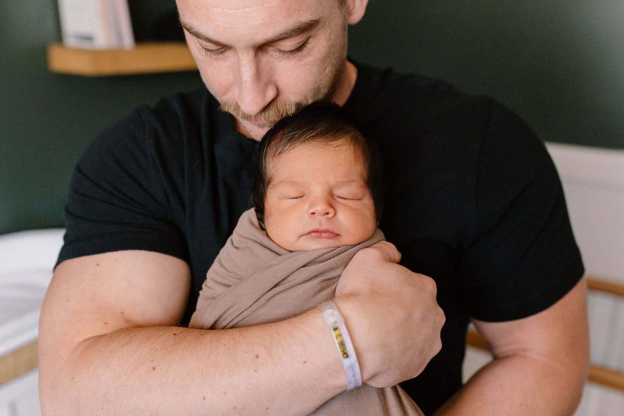 dad holding swaddled newborn baby in dark green nursery