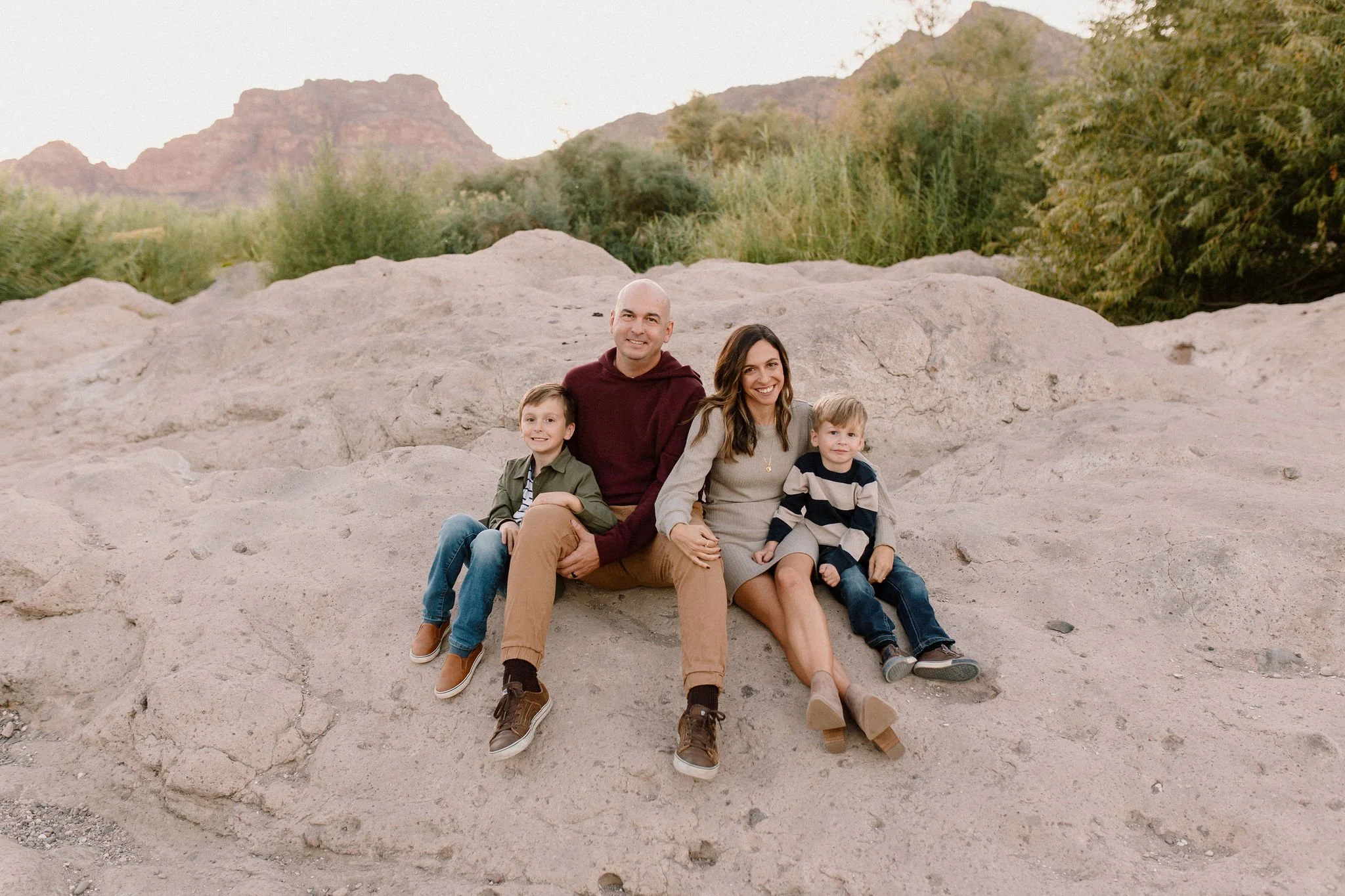 family sitting together and smiling on pink rocks near the Salt river with Red Mountain in the background