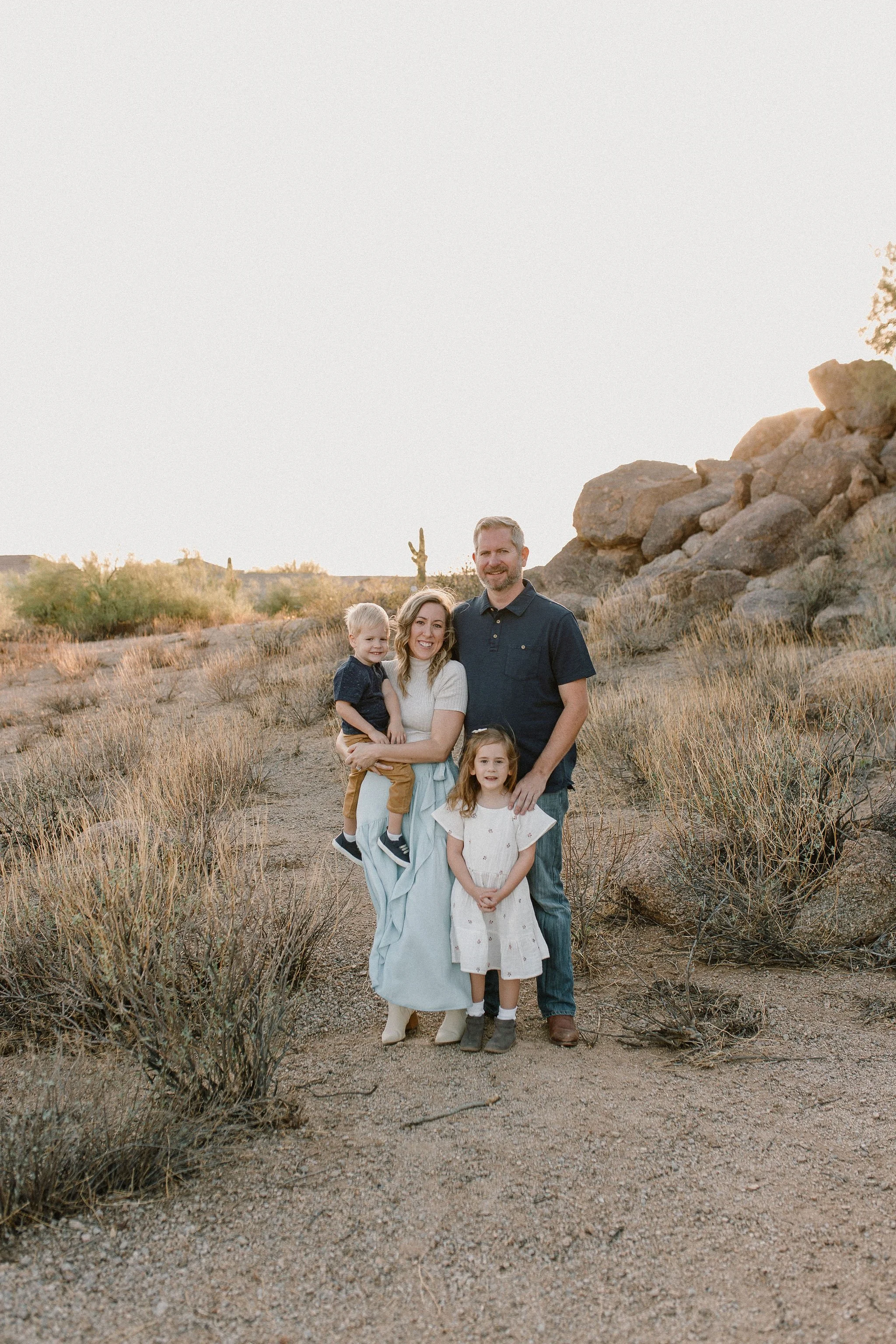 family standing together in the desert with large boulders and cacti smiling at mesa arizona family photographer