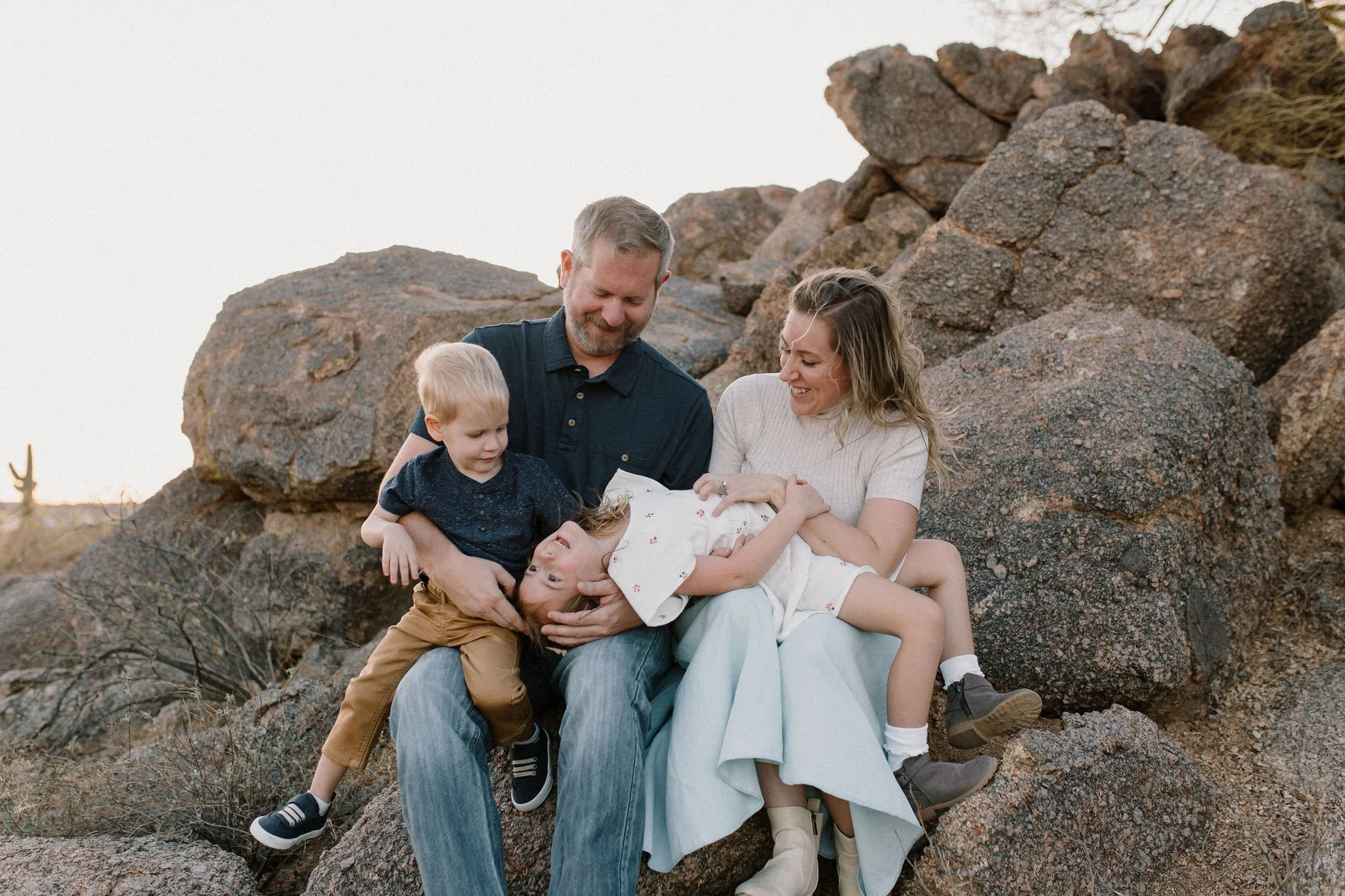 brother and sister siblings sitting and smiling on boulders in desert family photo session