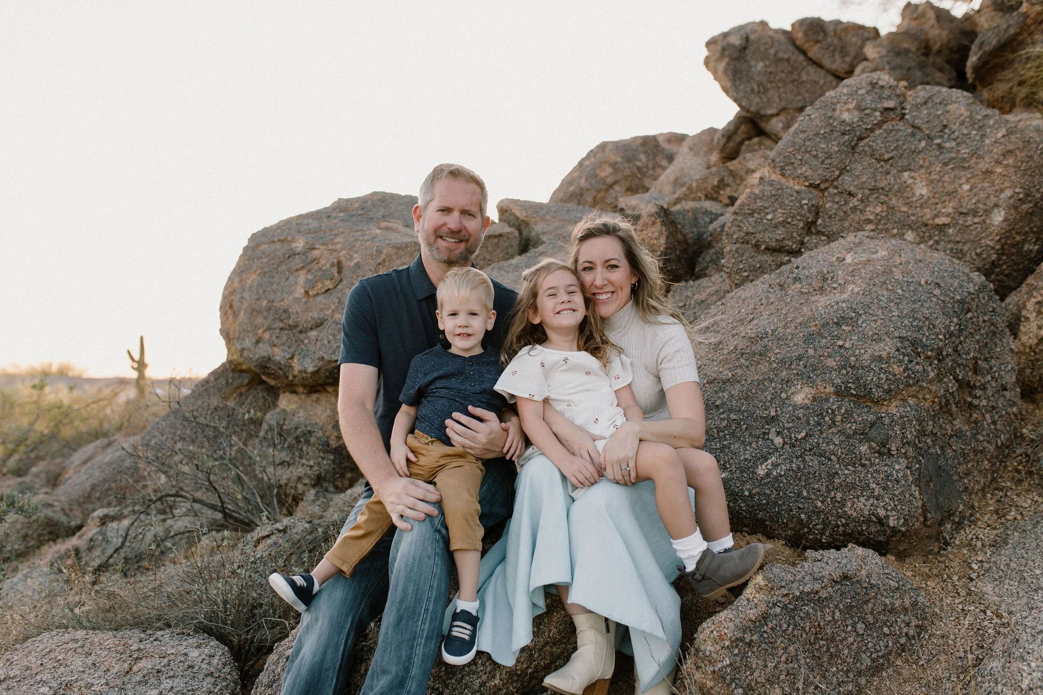 family sitting on boulders in the desert and smiling during windy family photoshoot