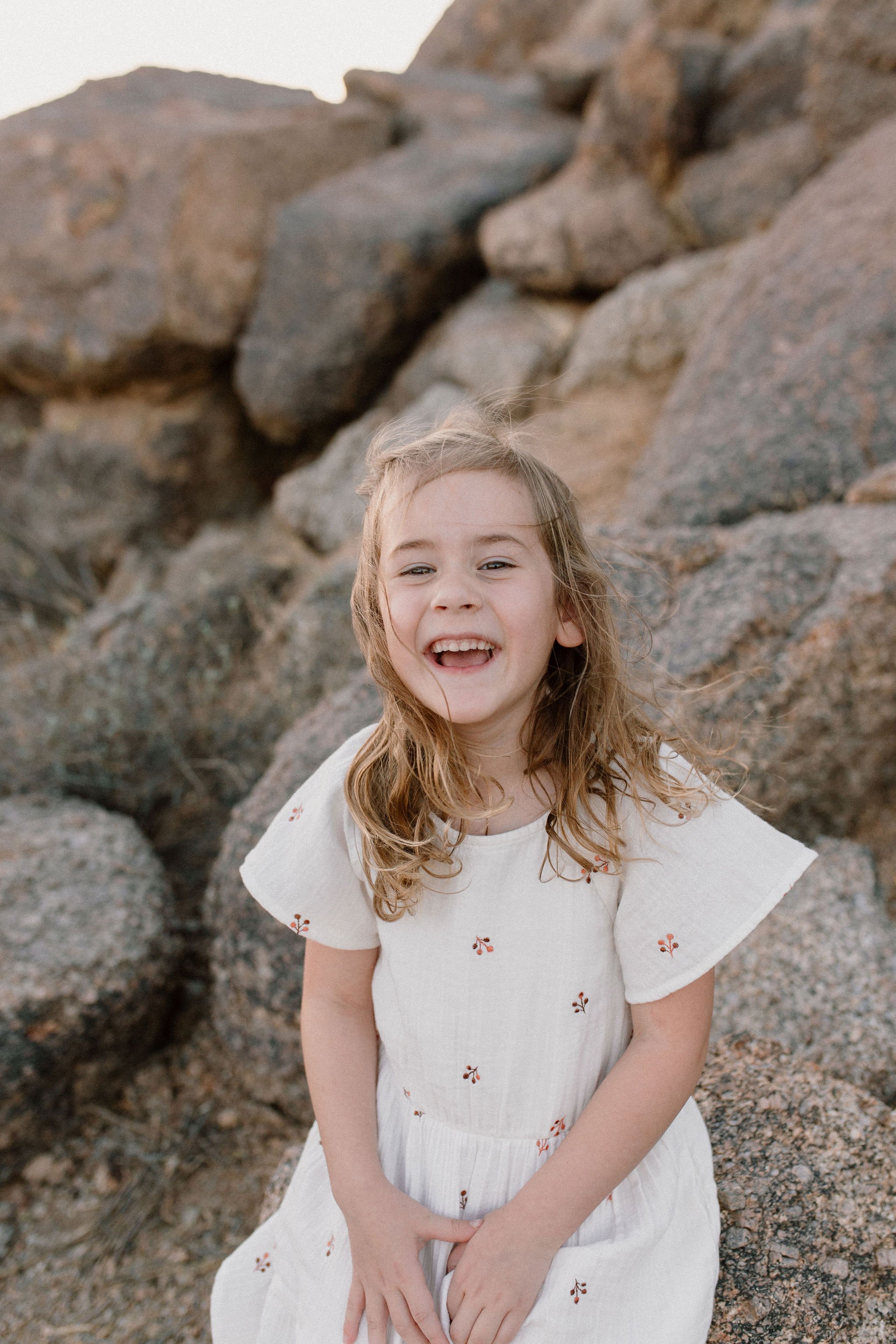 toddler daughter sitting on boulder in desert during windy family photo session