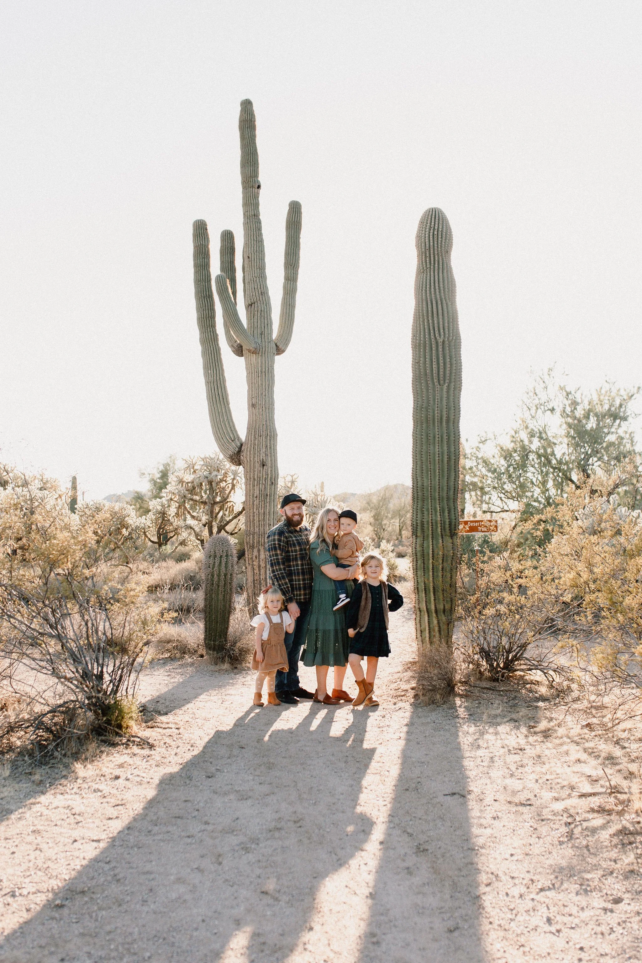 Family standing together smiling next to huge saguaro cactus in golden hour desert family photography session