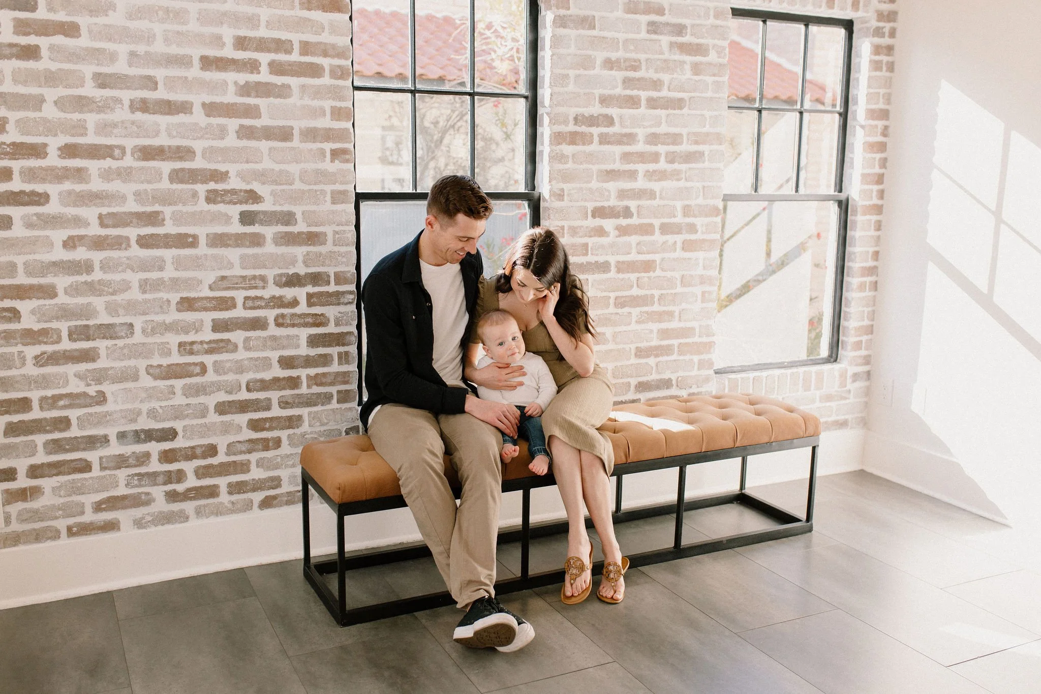 mom and dad holding baby boy in neutral studio with red brick wall in Phoenix, Arizona