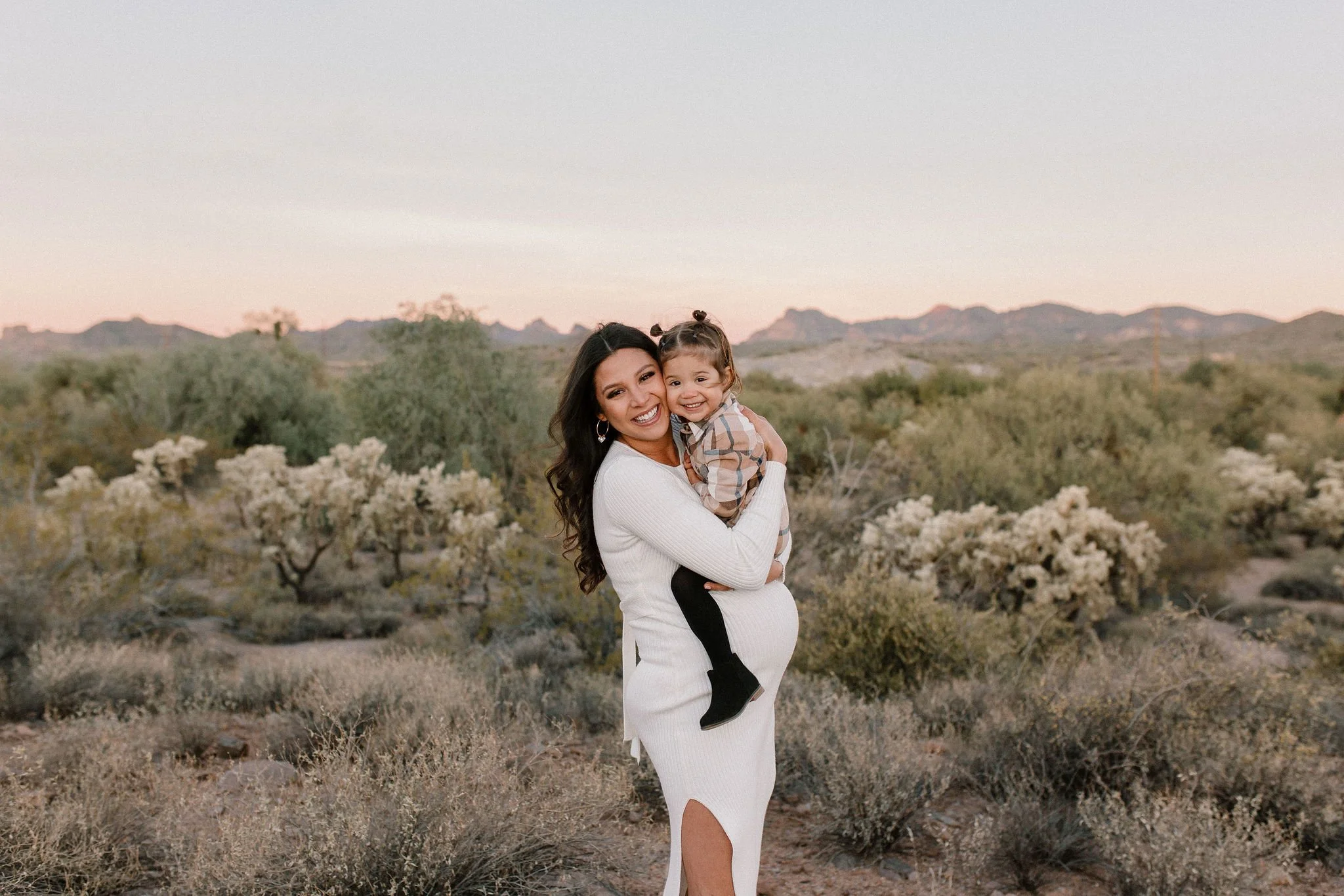 pregnant mom holding toddler daughter on her belly in desert family maternity pics in Lost Dutchman State Park