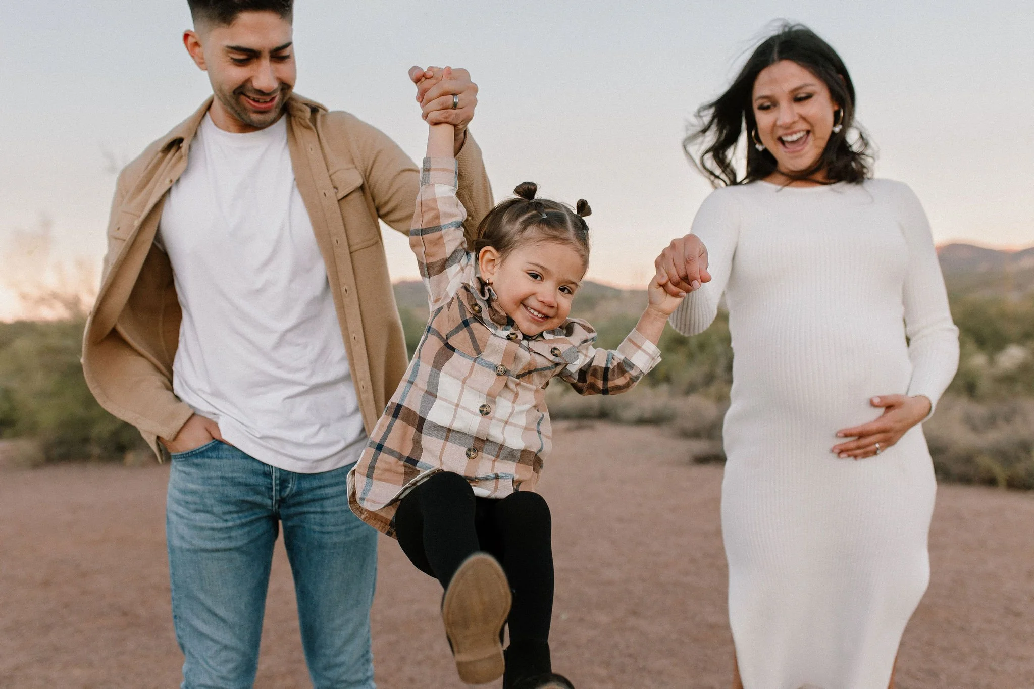 family walking and swinging toddler in the air in desert family maternity pics in Lost Dutchman State Park