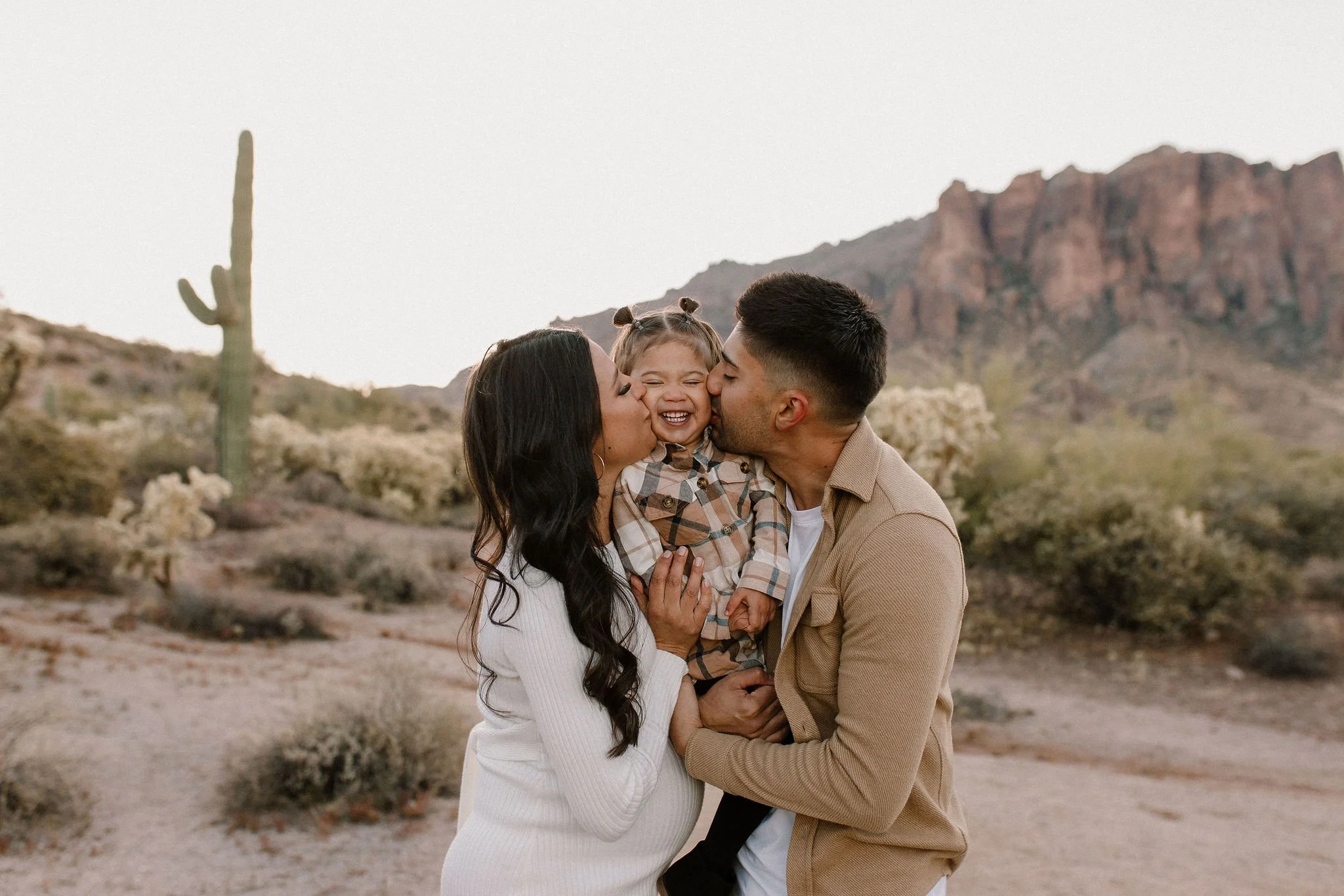pregnant mom and dad kissing toddlers cheeks in desert family maternity pics in Lost Dutchman State Park