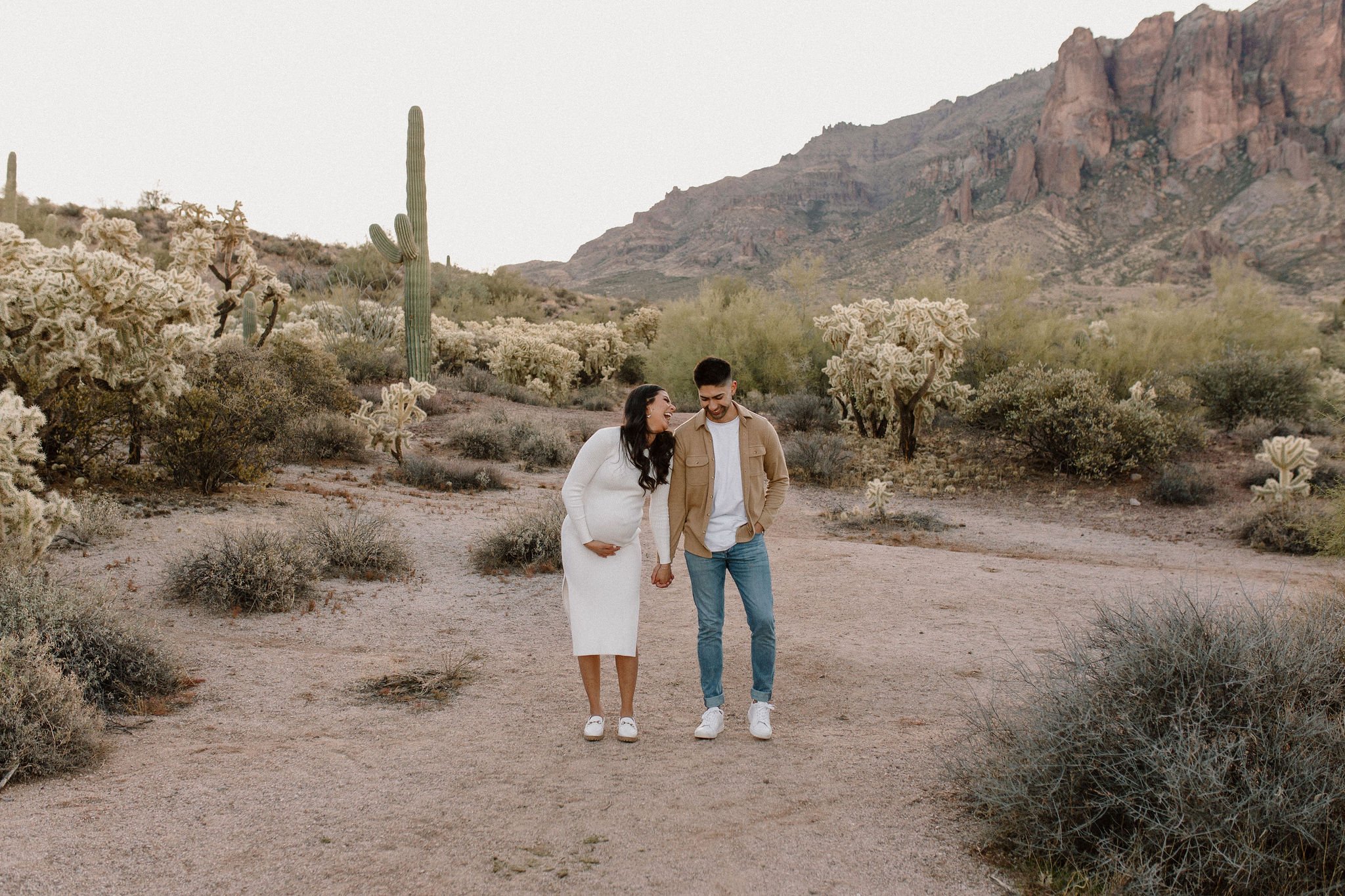 pregnant mom holding hands with dad laughing in desert family maternity pics in Lost Dutchman State Park