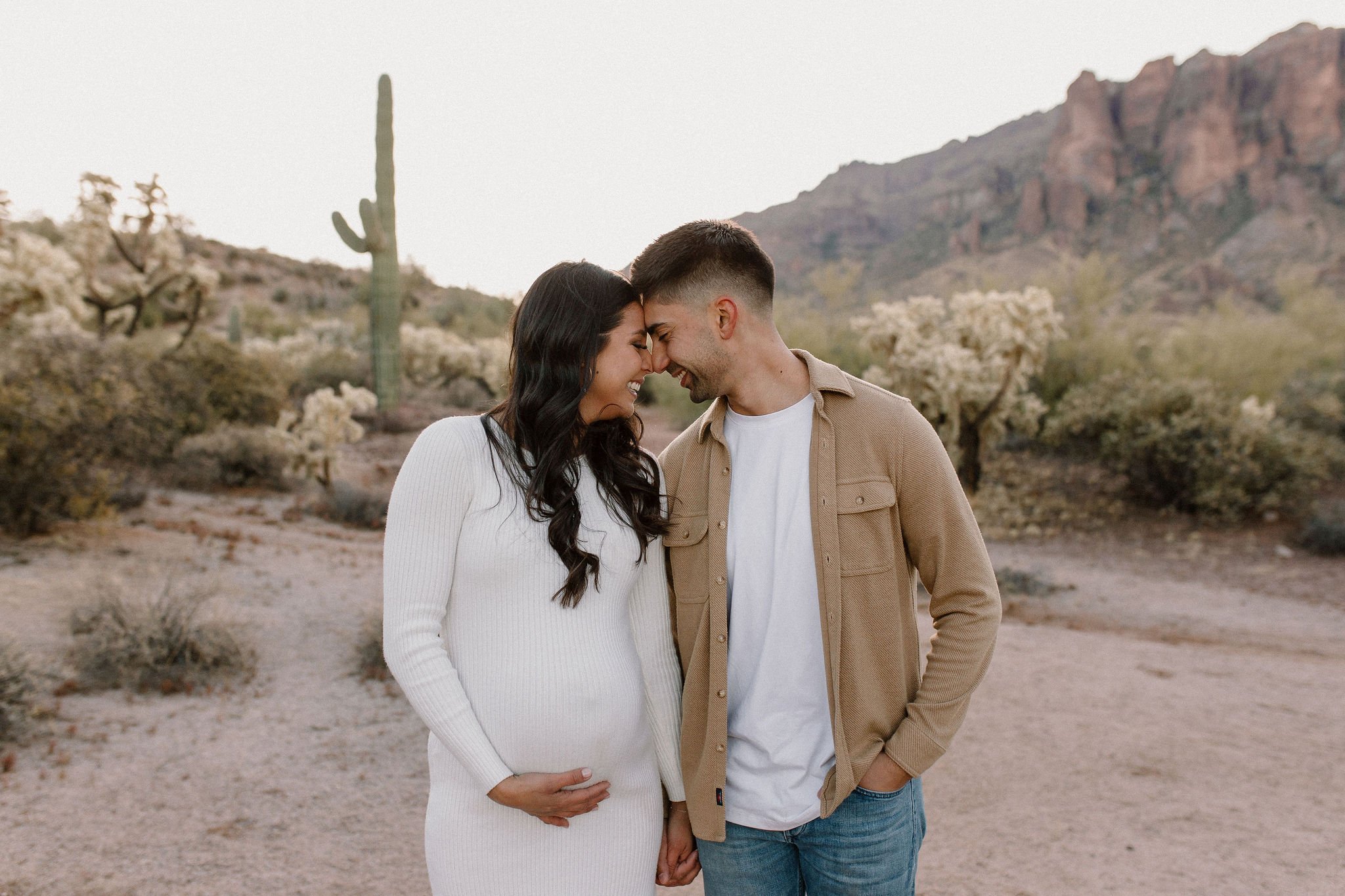 pregnant mom holding belly cuddling close to dad in desert family maternity pics in Lost Dutchman State Park