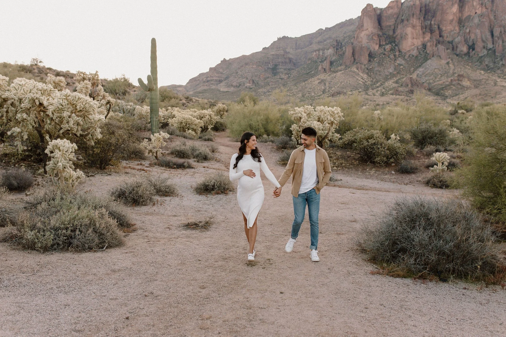 pregnant mom holding belly holding hands and walking with dad in desert family maternity pics in Lost Dutchman State Park