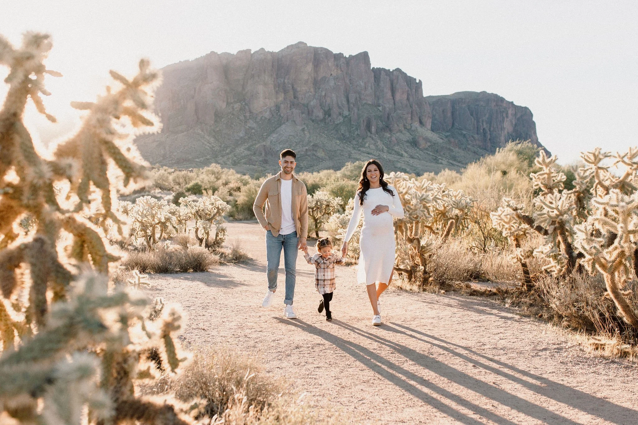 family holding hands walking and smiling in desert family maternity pics in Lost Dutchman State Park