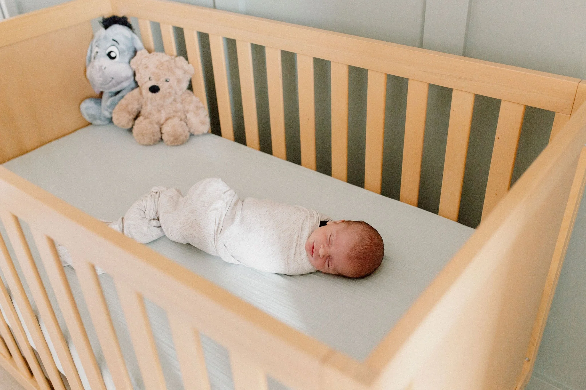swaddled newborn baby sleeping in neutral crib in nursery