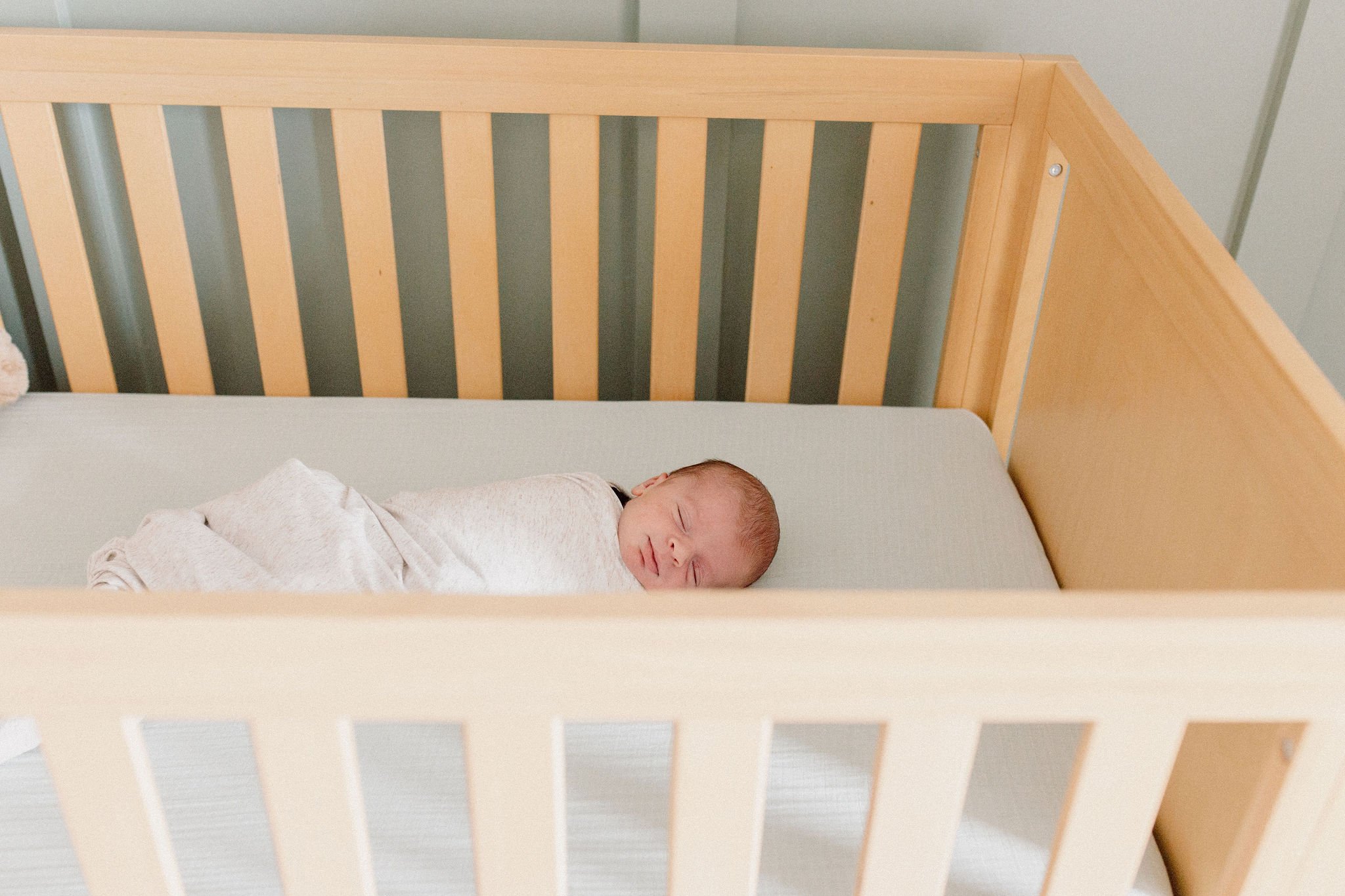swaddled newborn baby sleeping in crib in neutral nursery