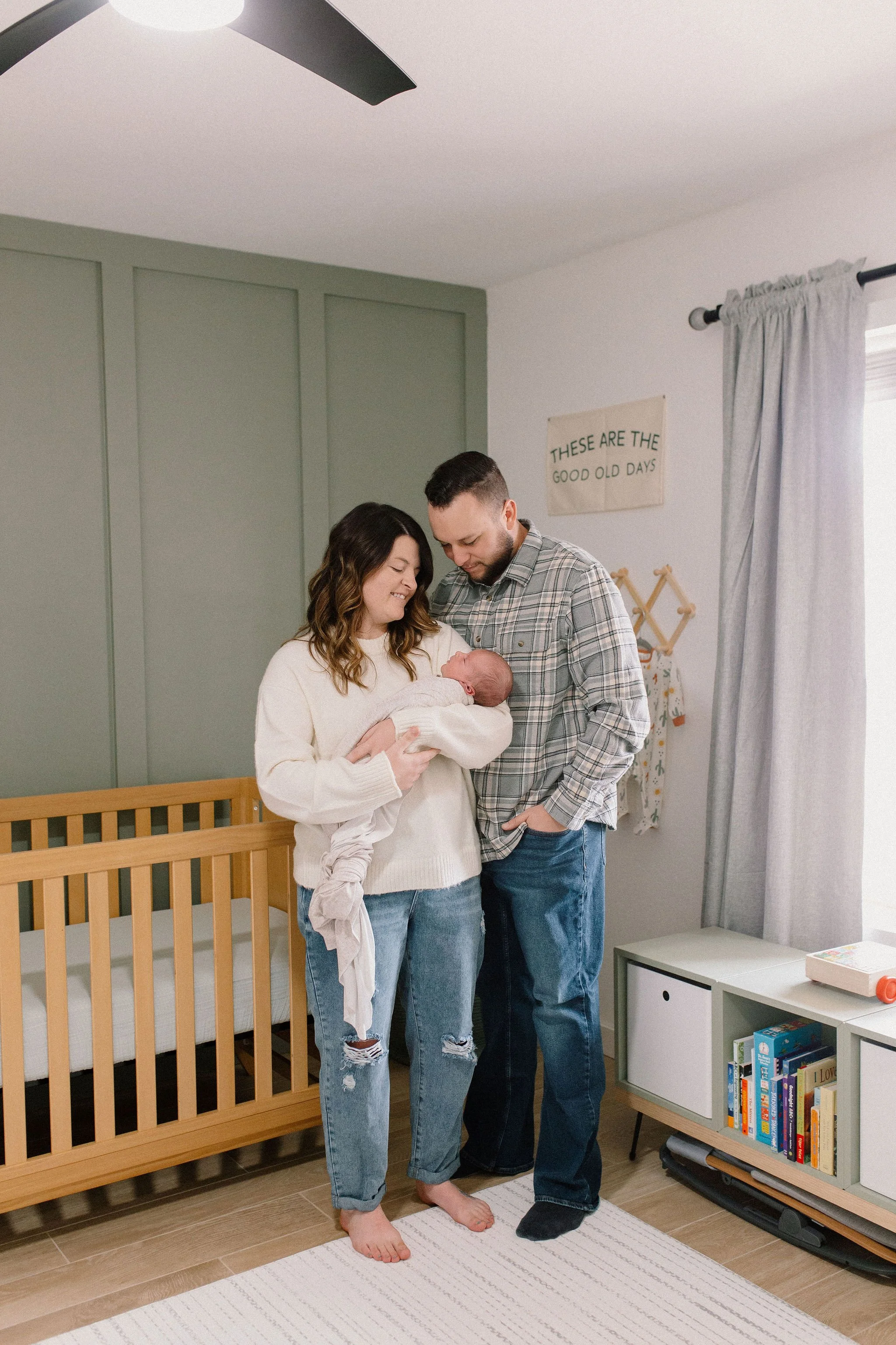mom and dad holding newborn baby in-home neutral nursery