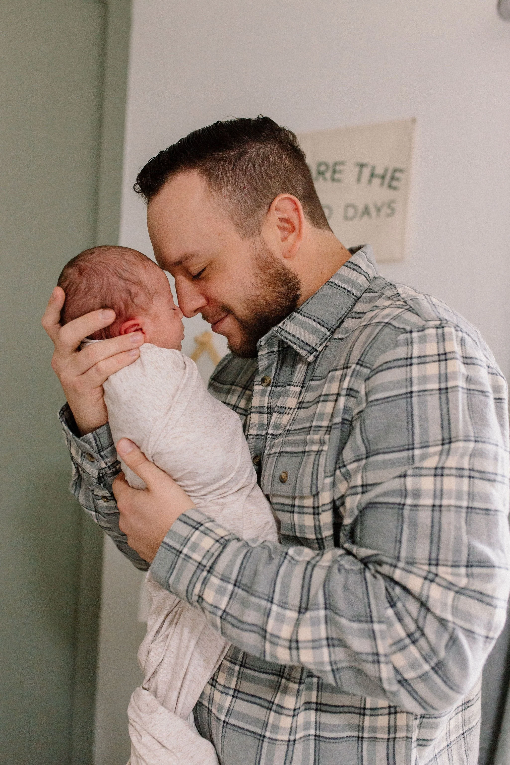dad holding swaddled newborn baby nose-to-nose in neutral nursery